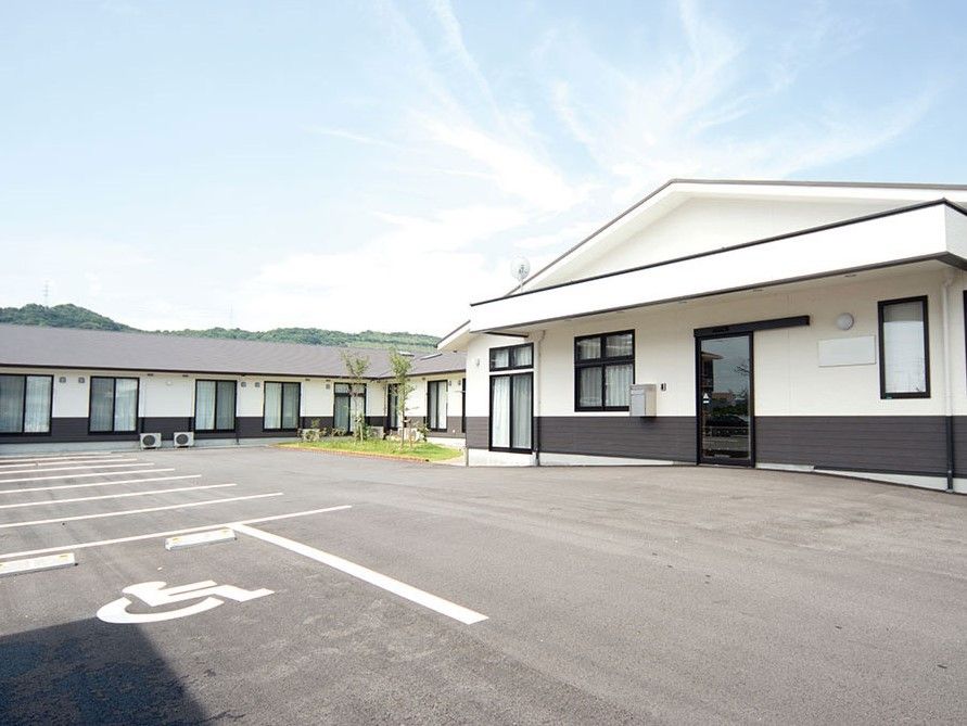 広い駐車場を備えた平屋建ての住宅。白とグレーの落ち着いた雰囲気の建物。