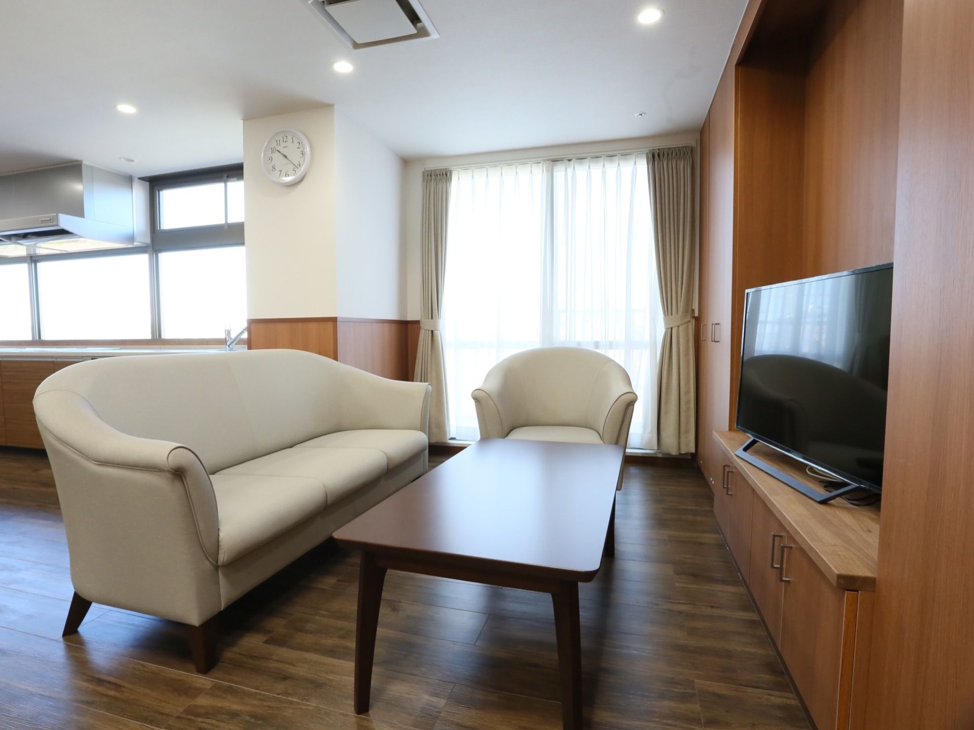 茶色い棚に設置されたテレビの前にテーブルがある。テーブル周りには3人掛けと1人掛けのソファーが用意されている。