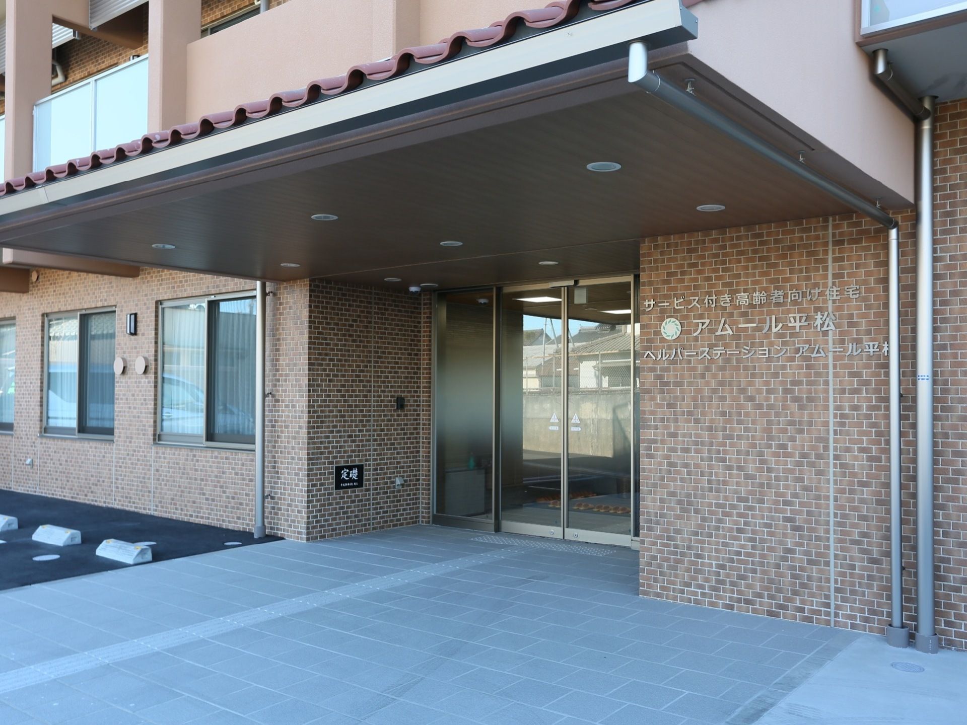 大きなひさしが設置された玄関で、ひさしには丸型の小型ライトが複数取りつけられている。玄関のドアは自動ドアになっている。