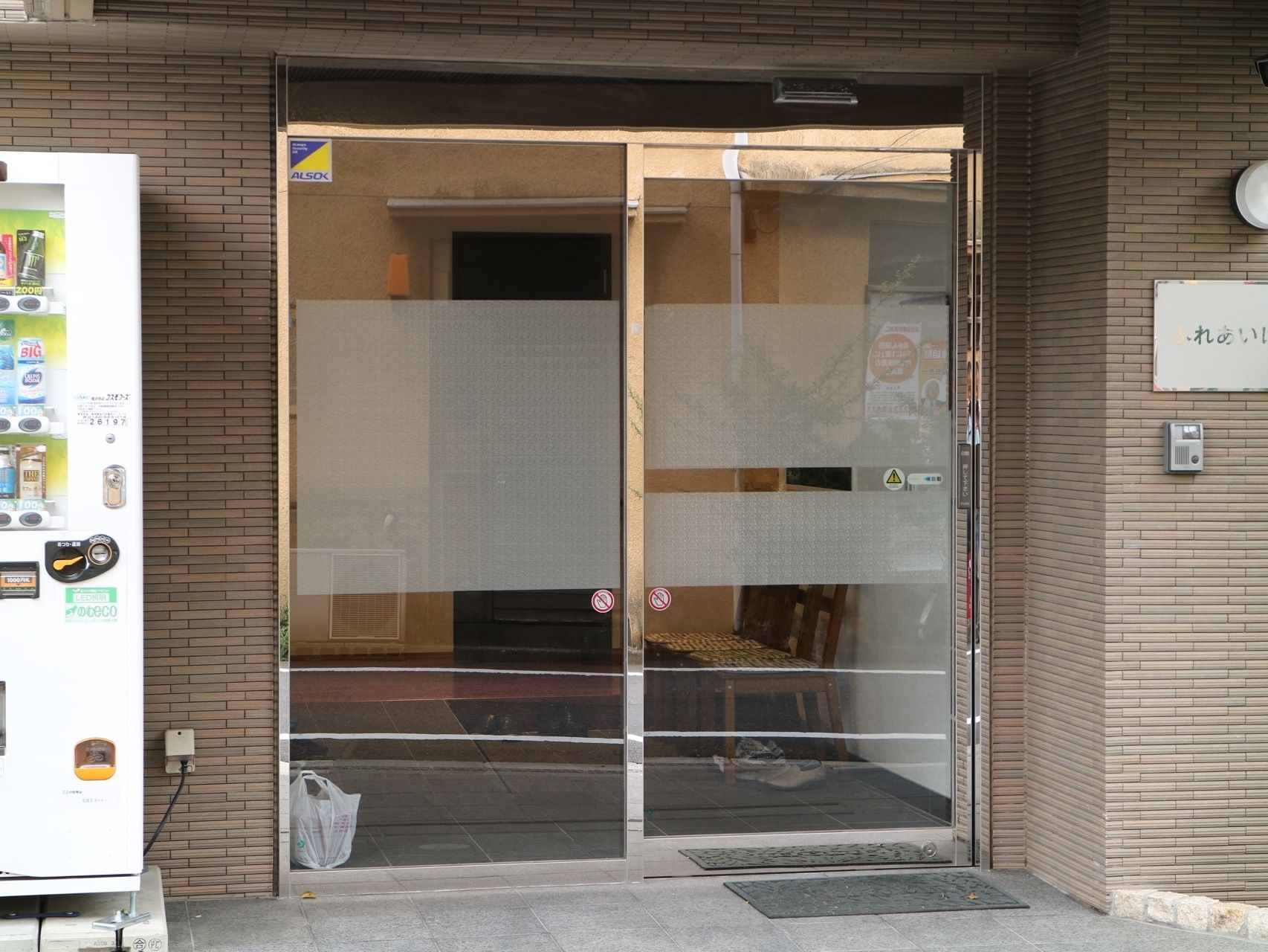 玄関横の壁には、施設名が書かれている。外から段差なく入れる玄関は、ガラス張りの大きな自動ドアになっている。