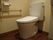 白を基調とした、掃除が行き届き清潔なトイレである。手すりを設けることで、立ち座りの動作で負担を軽減している。