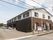 横幅の広い2階建ての施設が建っており、前面にはアスファルトで舗装された駐車場が広がっている。フェンスの手前には道路が見える。