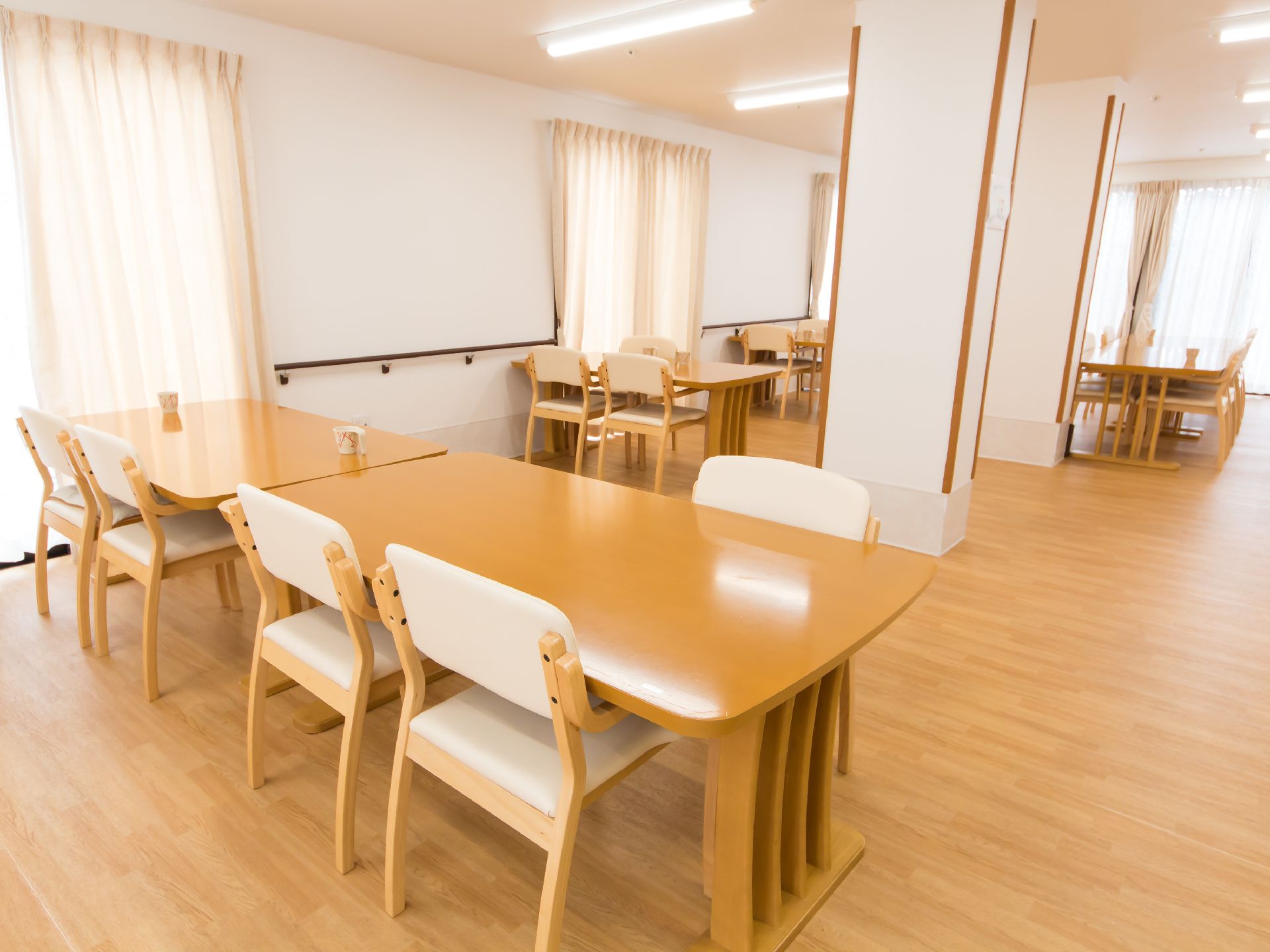 大きめの窓が複数ついた食堂は日当たり良好。4人掛けのテーブルが複数置かれている。