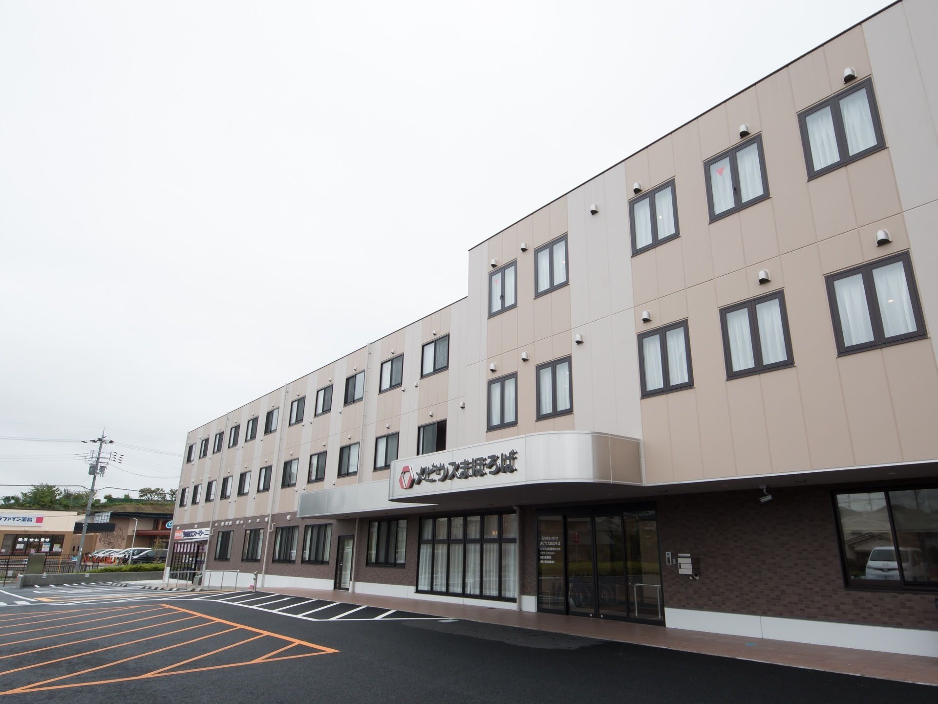 ピンク系の外壁の３階建ての建物で、敷地内はきれいに舗装されている。１階部分は茶色のレンガの壁になっている。