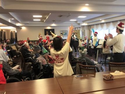 共有スペースに集まりクリスマス会を楽しむ入居者と、会を盛り上げるスタッフ。