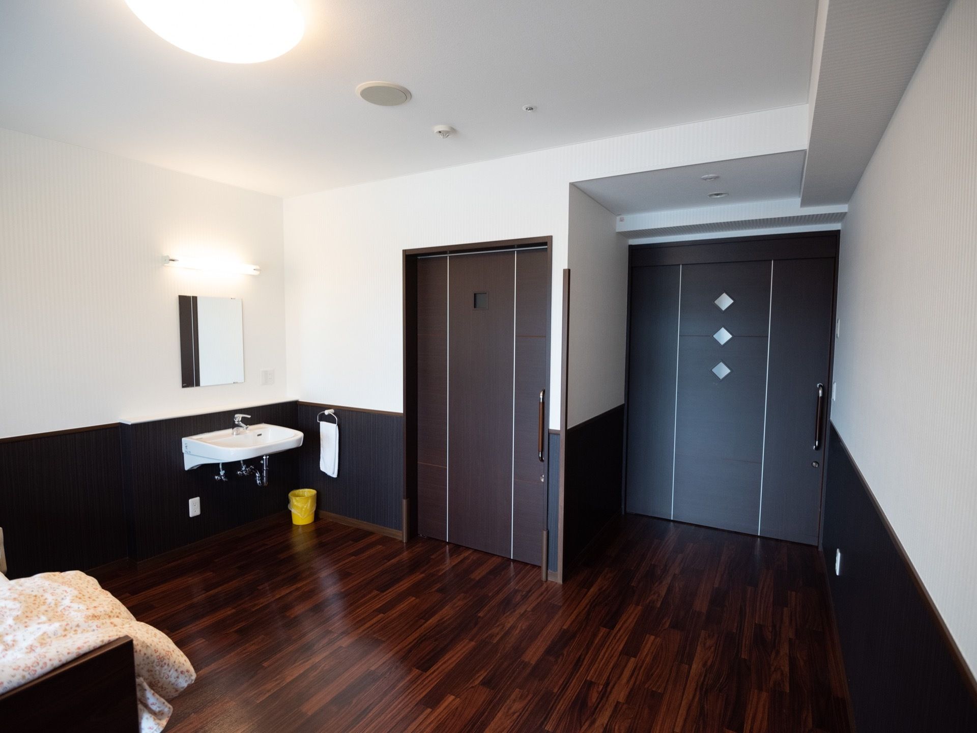 モダンなデザインの居室である。洗面台や介護ベッド、トイレが完備されている。スライドドアが出入り口の扉として採用されている。