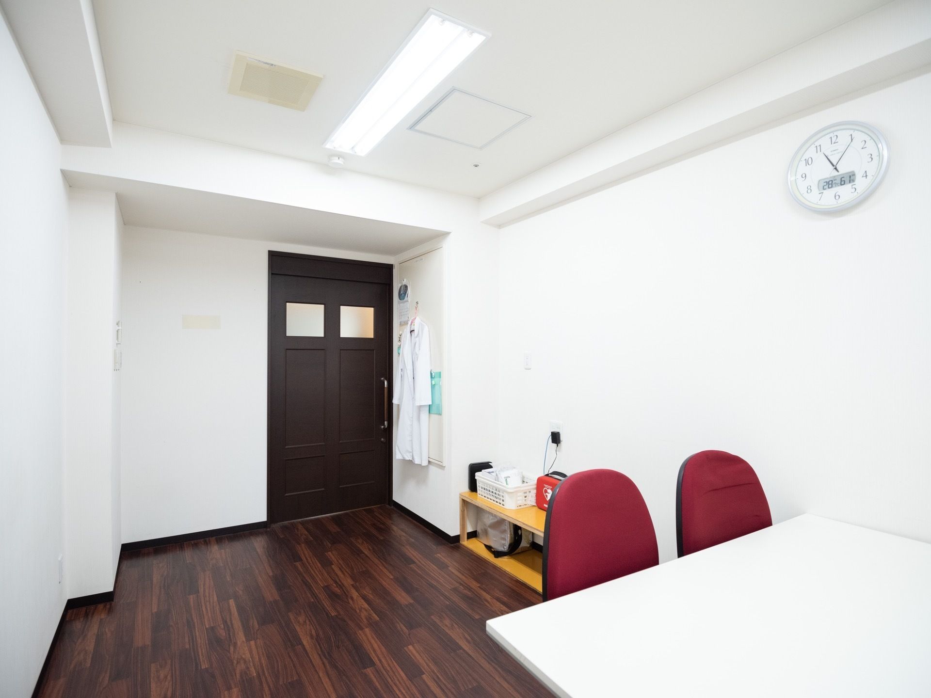 医務室はスッキリとした明るい部屋である。出入り口近くの壁には、白衣が掛けられている。黄色い棚の上には、AEDが置かれている。