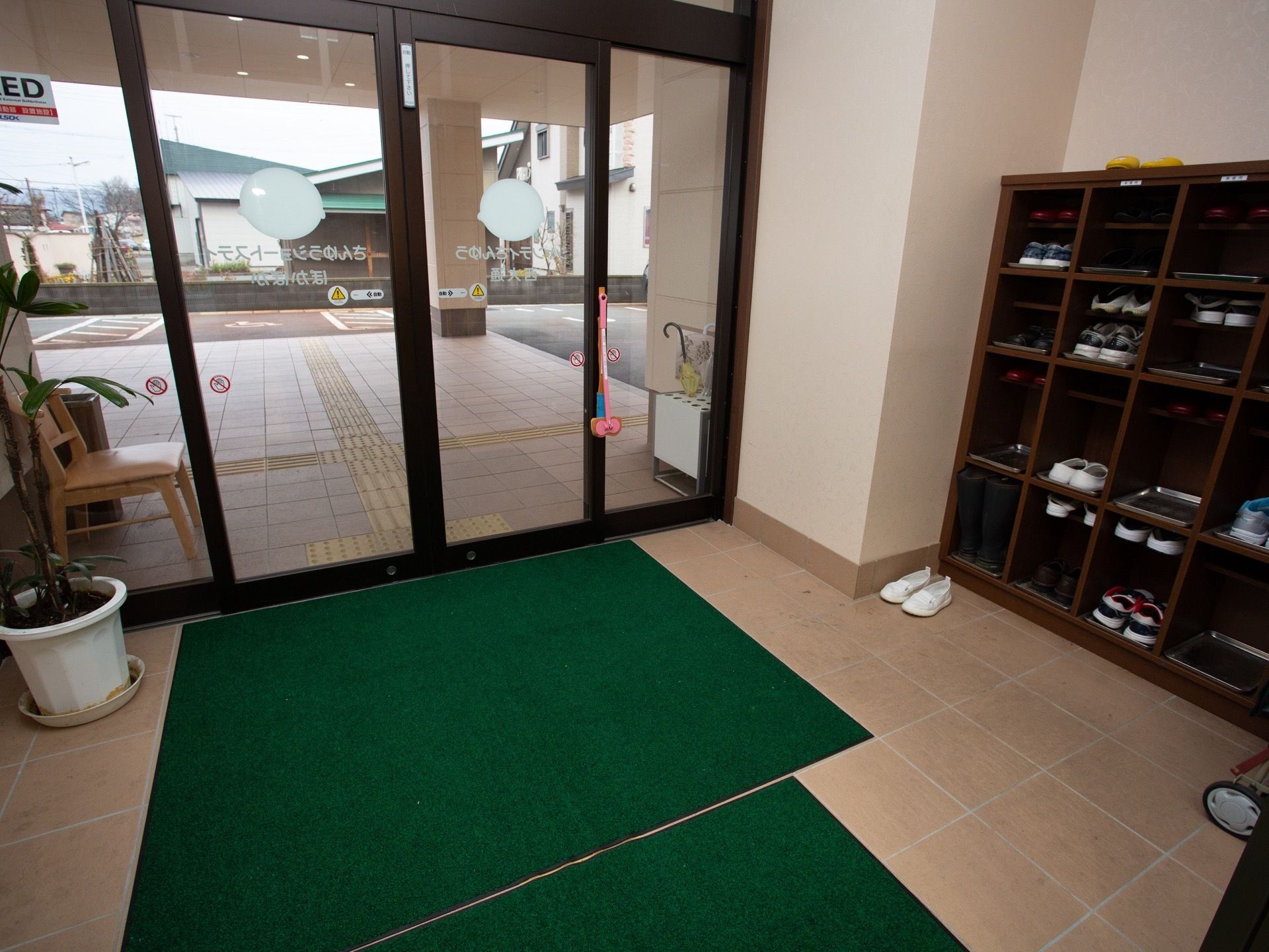 玄関には緑色の玄関マットが敷かれている。入り口は自動扉になっており、観葉植物が飾られている。下駄箱には靴が収納されている。
