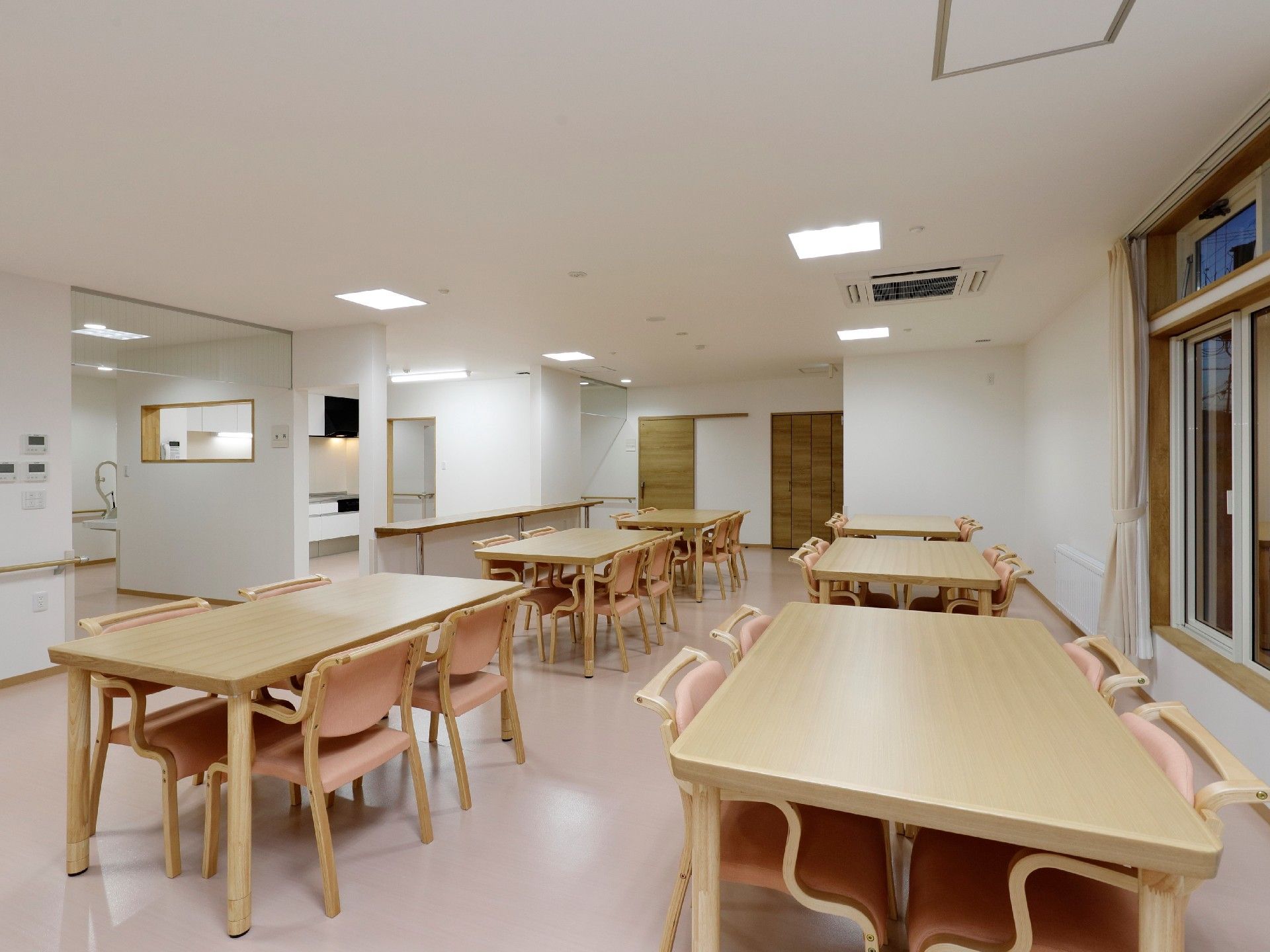 木製のテーブルセットが複数置かれた明るい食堂。窓が大きく、日当たりもよい。