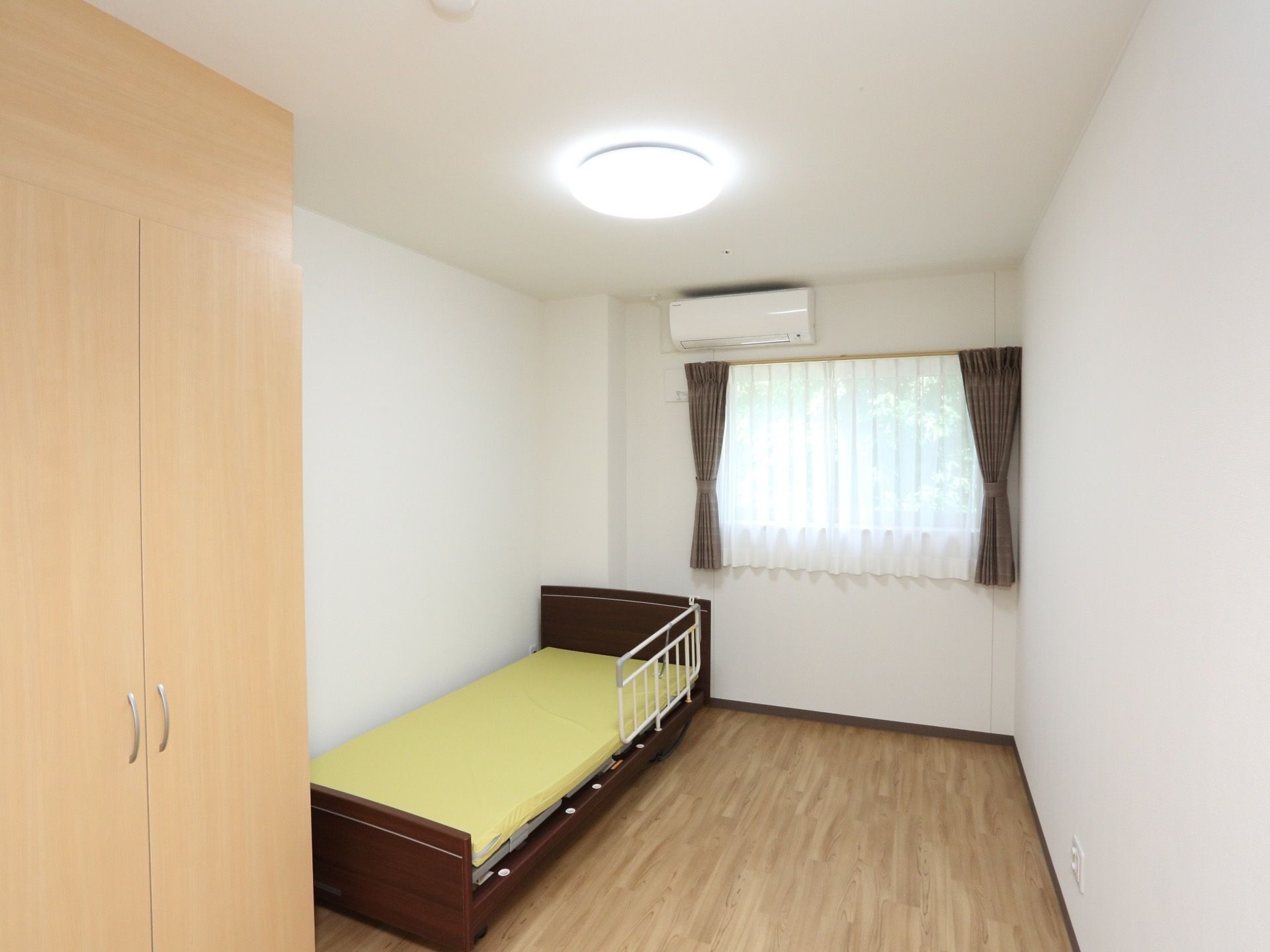真っ白い部屋で丸い照明が天井に設置されている。木製のサイドレールのついた電動ベッドが用意されている。