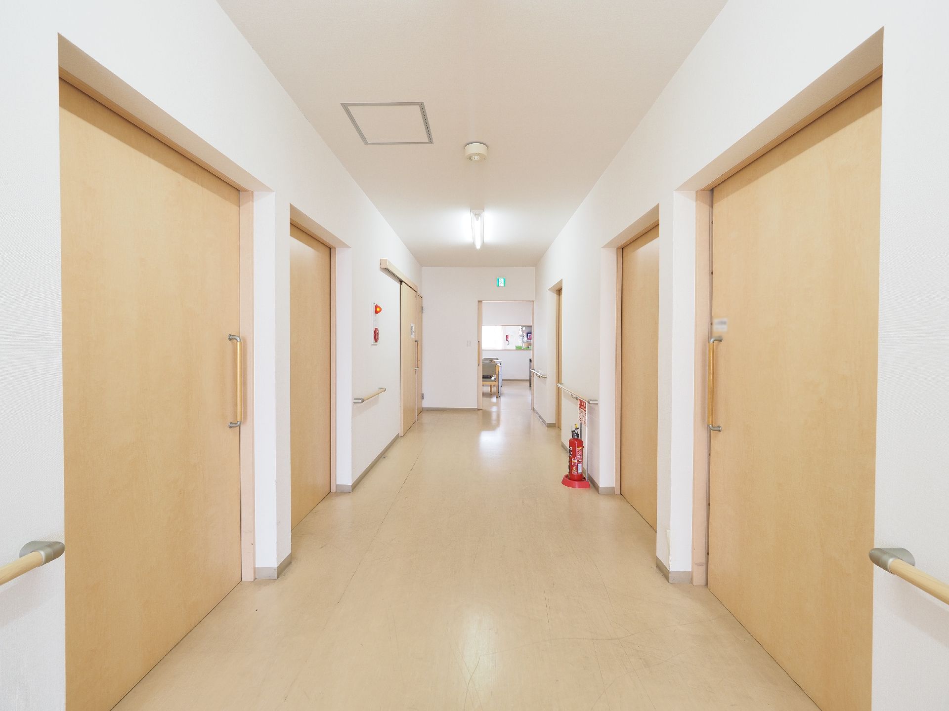 白い壁にフローリングの廊下が続いている。壁には手すりがついていて、各部屋の扉は大きな引き戸になっている。