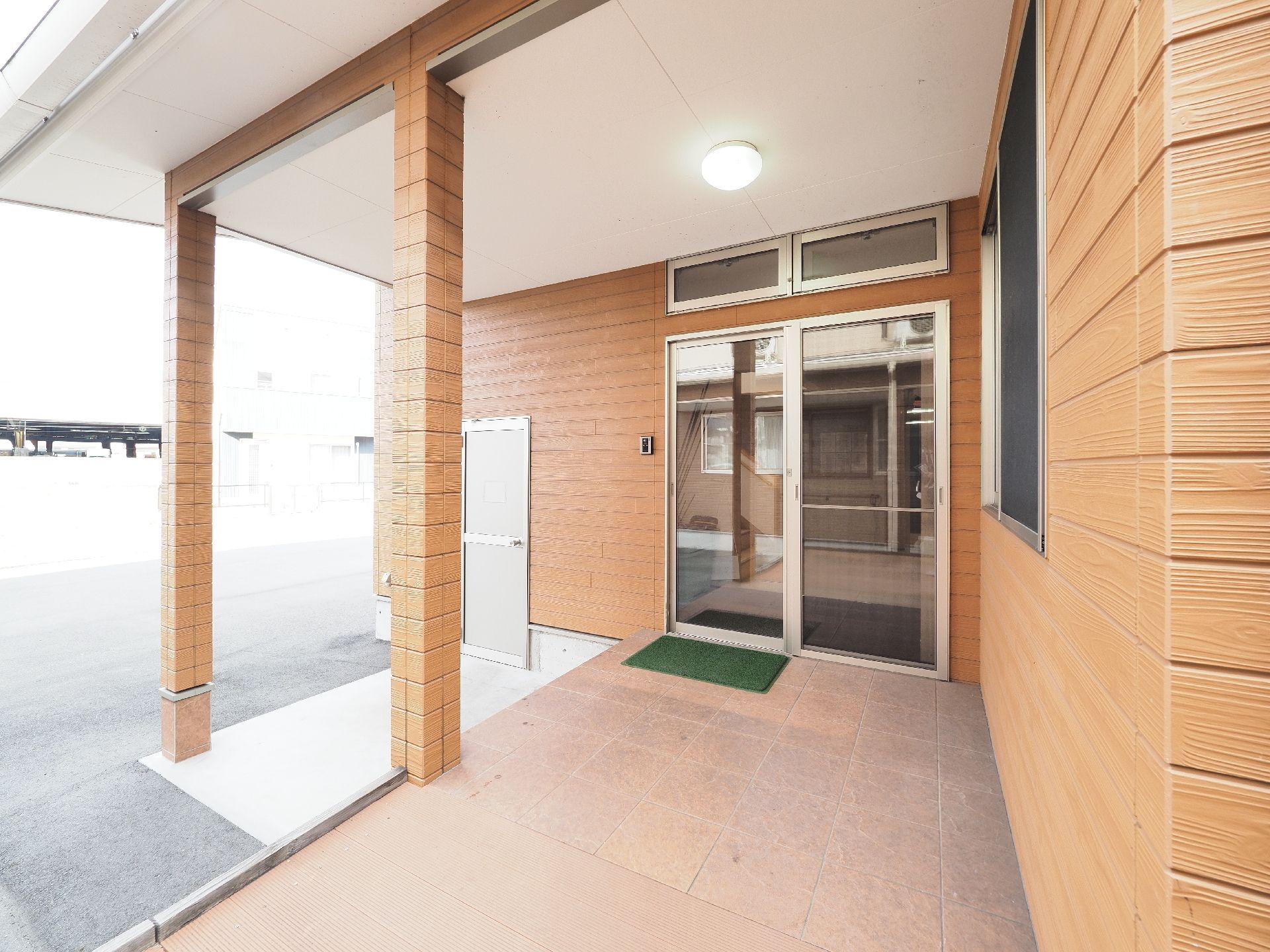 木目調のタイルが貼られた建物で、玄関には屋根がついている。玄関の扉までは緩やかなスロープになっている。