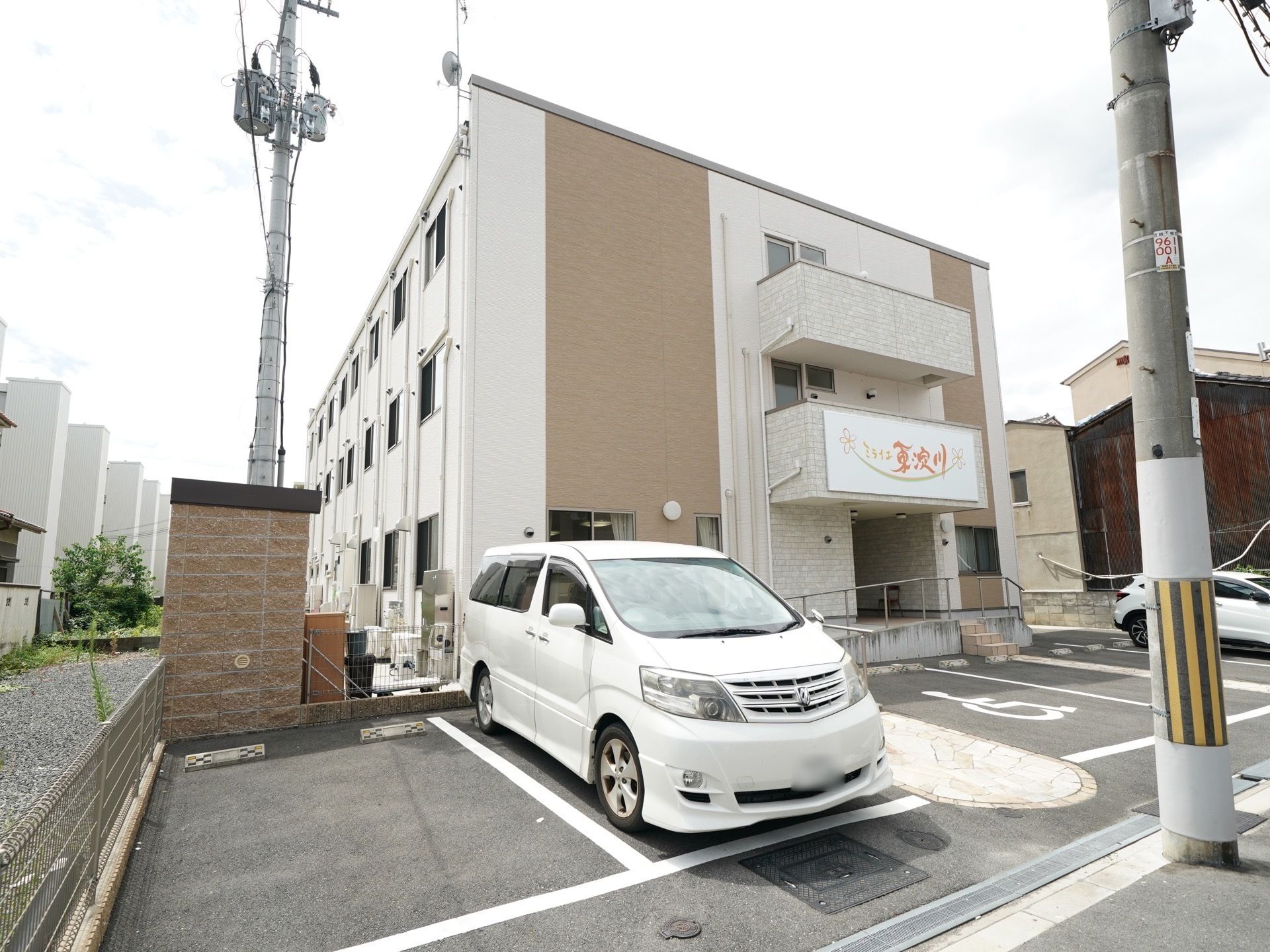 建物のそばに駐車スペースがある、３階建ての施設の外観