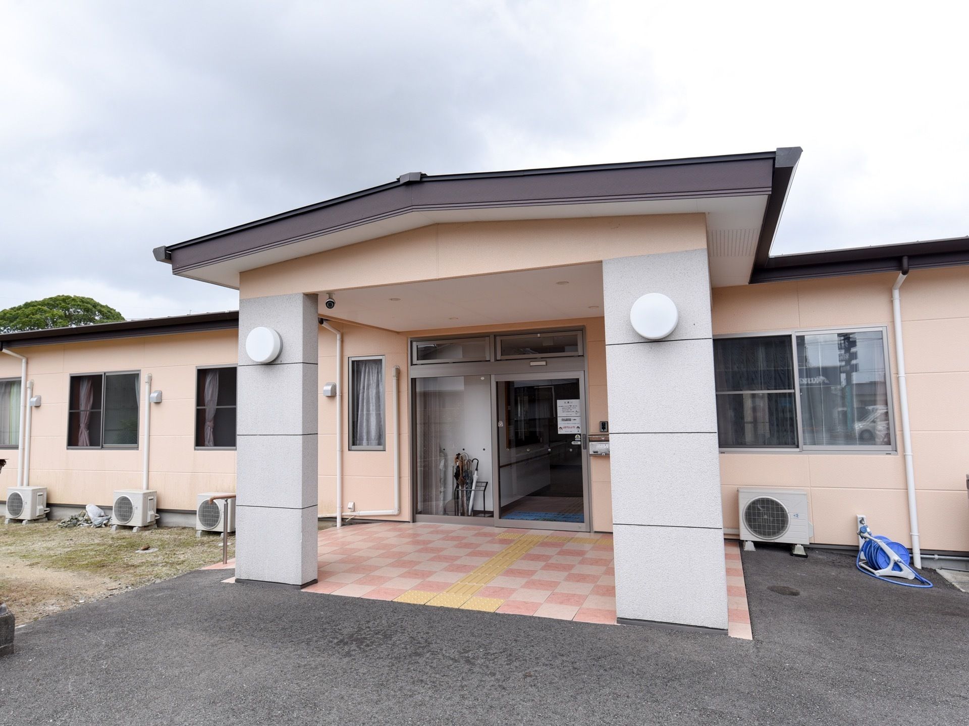 建物はうすいピンク色の壁の平屋建てで、玄関ドアはガラス張りの自動ドアになっている。大きなルーフがある。