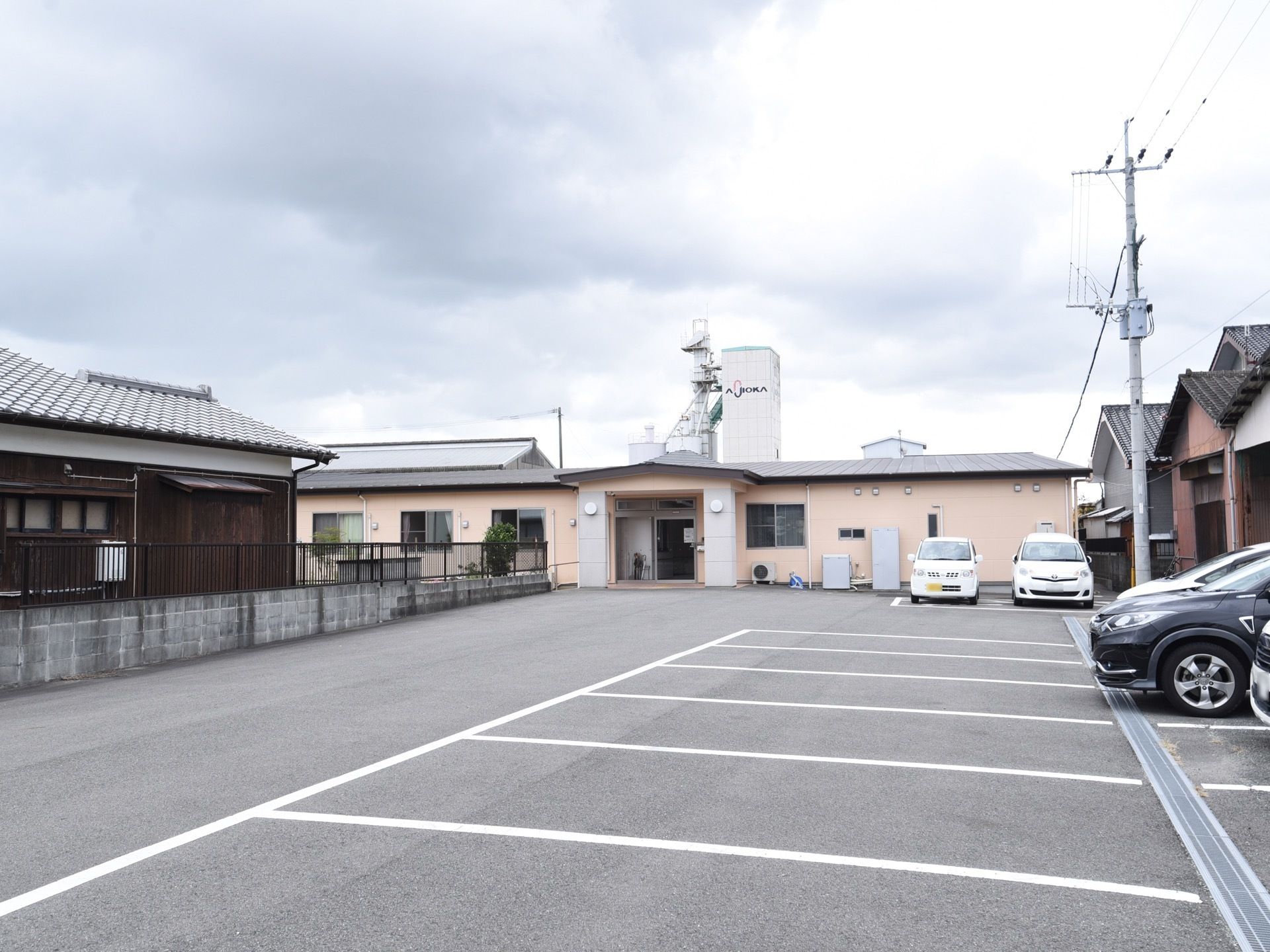施設の建物は、前面が広い駐車場になっている。地面は舗装され、駐車スペースは白線で区切られている。隣家との間に低い塀が設けられている。