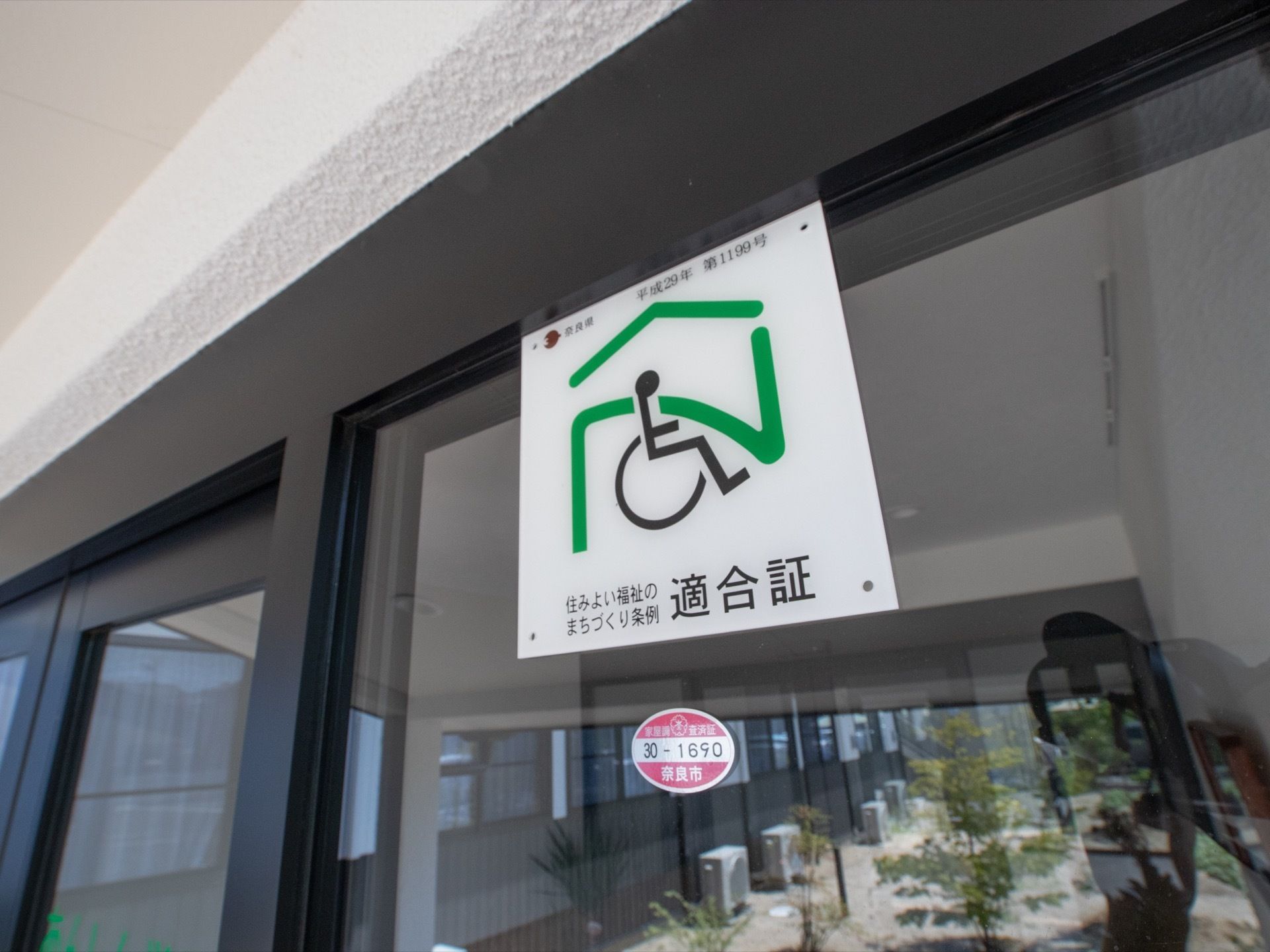 建物の窓の隅に貼られたステッカーが映っている。車椅子の描かれたマークには、条例の適合証と書かれている。