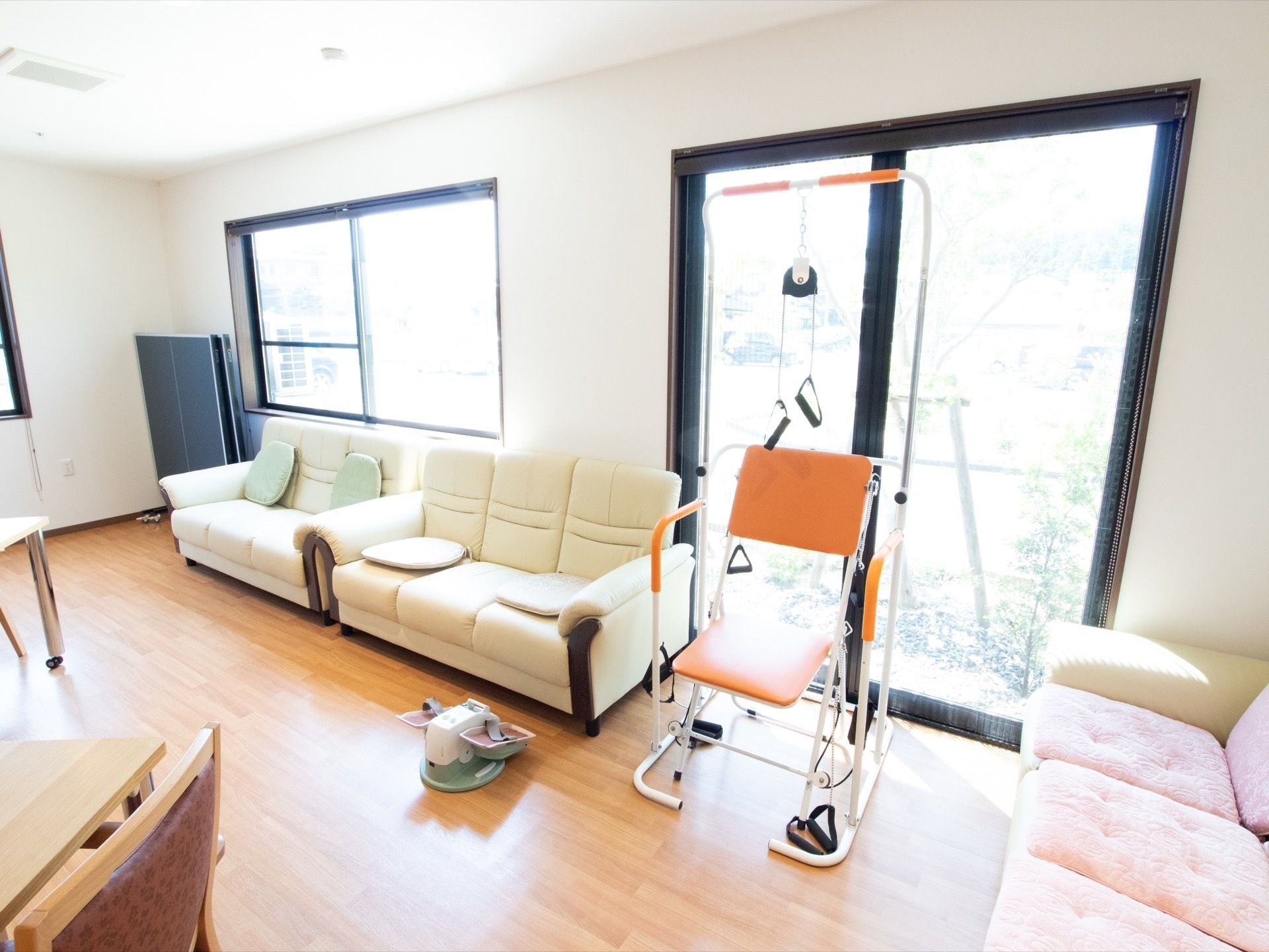 室内には大きな窓が３つ見える。奥のソファの隣には、折り畳まれた卓球台が置かれている。窓の外は庭になっている。