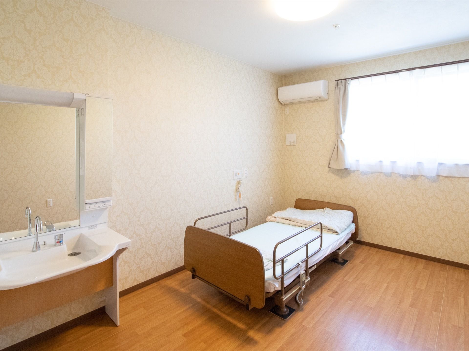 介護用ベッドの傍らにはスタッフ呼出ボタンを備える。窓のそばにはエアコンも完備されており、快適に過ごすことができる。