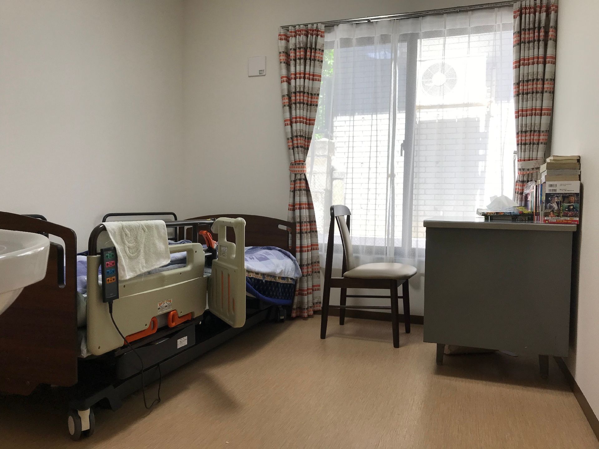 居室にはベッドが置かれ、デスクといすもある。窓は大きく、ストライプ模様のカーテンが付けられている