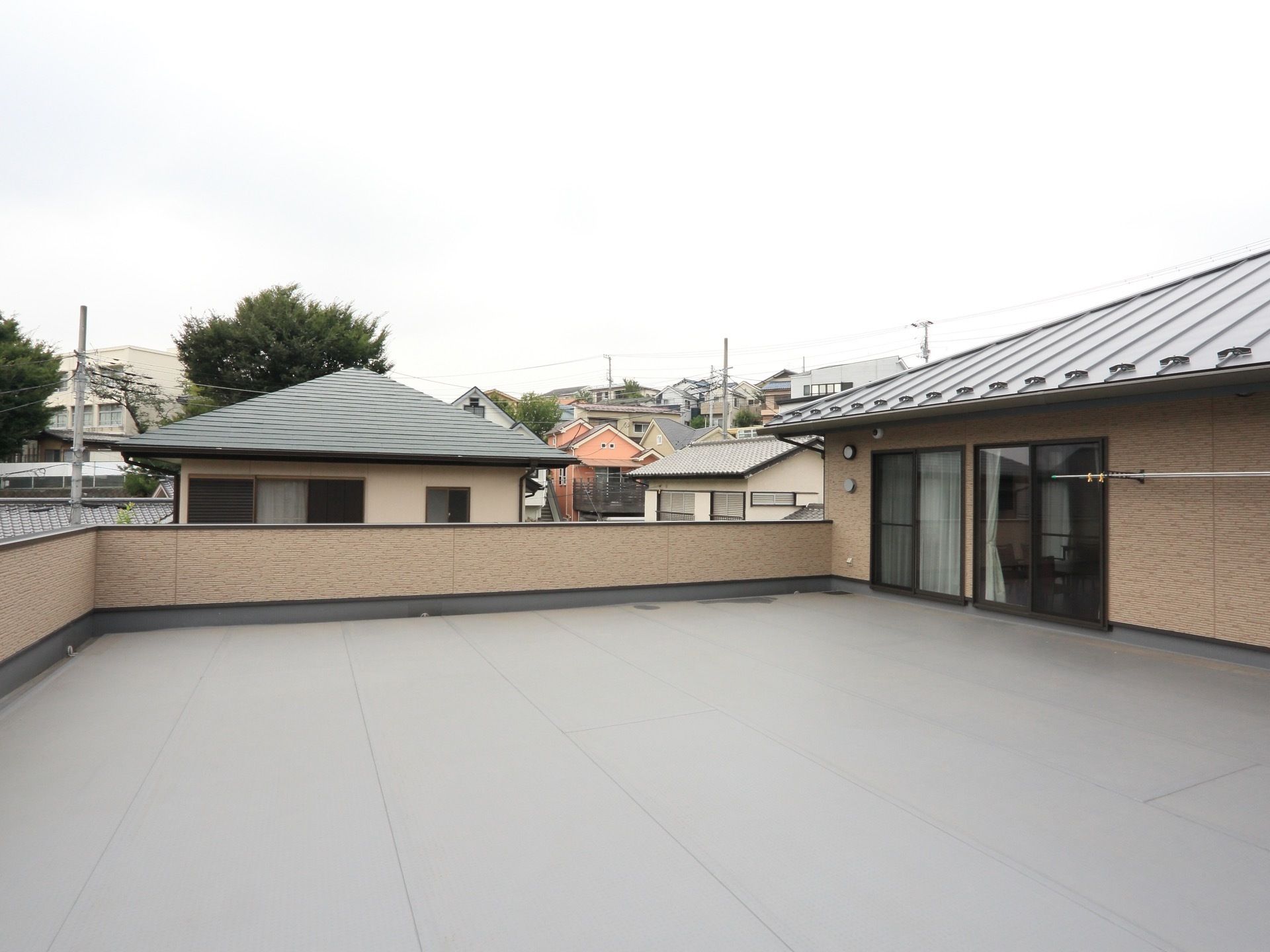 障害物がない広々とした屋上で、壁沿いに物干し竿が設置されている。周辺は住宅街が広がっているのが分かる。