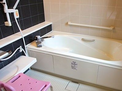 一般的な家庭と同じようなサイズの浴室。白い浴槽の横には手すりが設置され、呼び出しボタンもある。シャワーの前にはシャワーチェア。