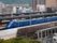 駅周辺の様子。青い電車が止まり、駅周辺には高層ビルが多く建ち並んでいる。