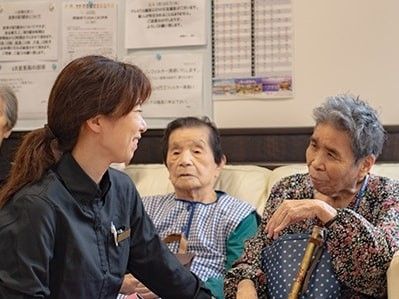 ソファに座った女性入居者と女性スタッフがにこやかに談笑している様子。