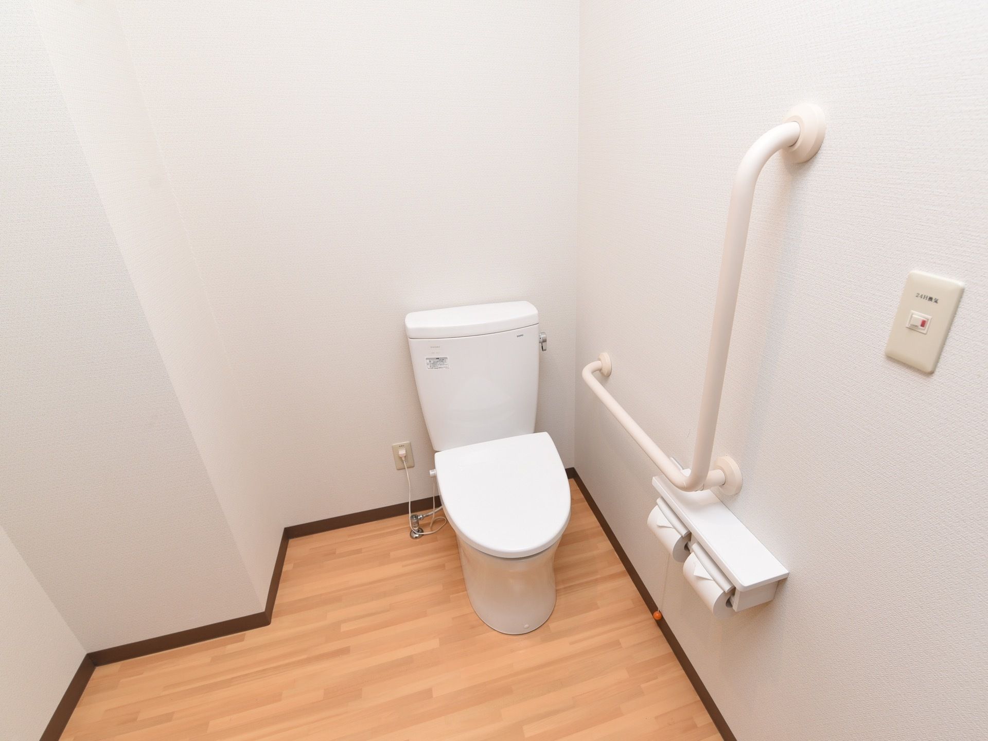白い壁の清掃の行き届いたきれいなトイレである。Ｌ字型の手すりを壁に設置しており、体を支えながら安全に利用することができる。