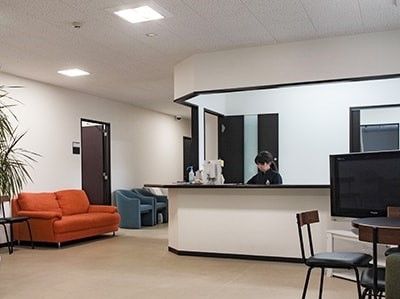 フロントに常駐するスタッフ。オープンで話しかけやすい雰囲気。近くにはソファやテレビスペースがある。