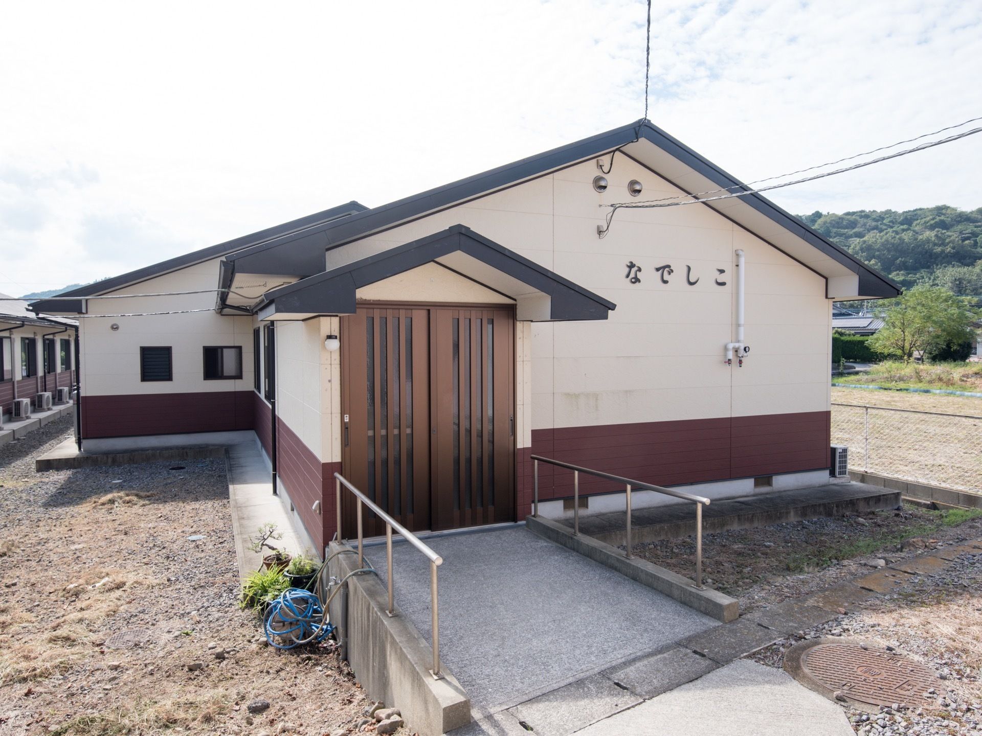 平屋建ての施設の外壁には施設名がブラウンの文字で書かれている。周りには木々などの自然が多くあり、静かな環境である。