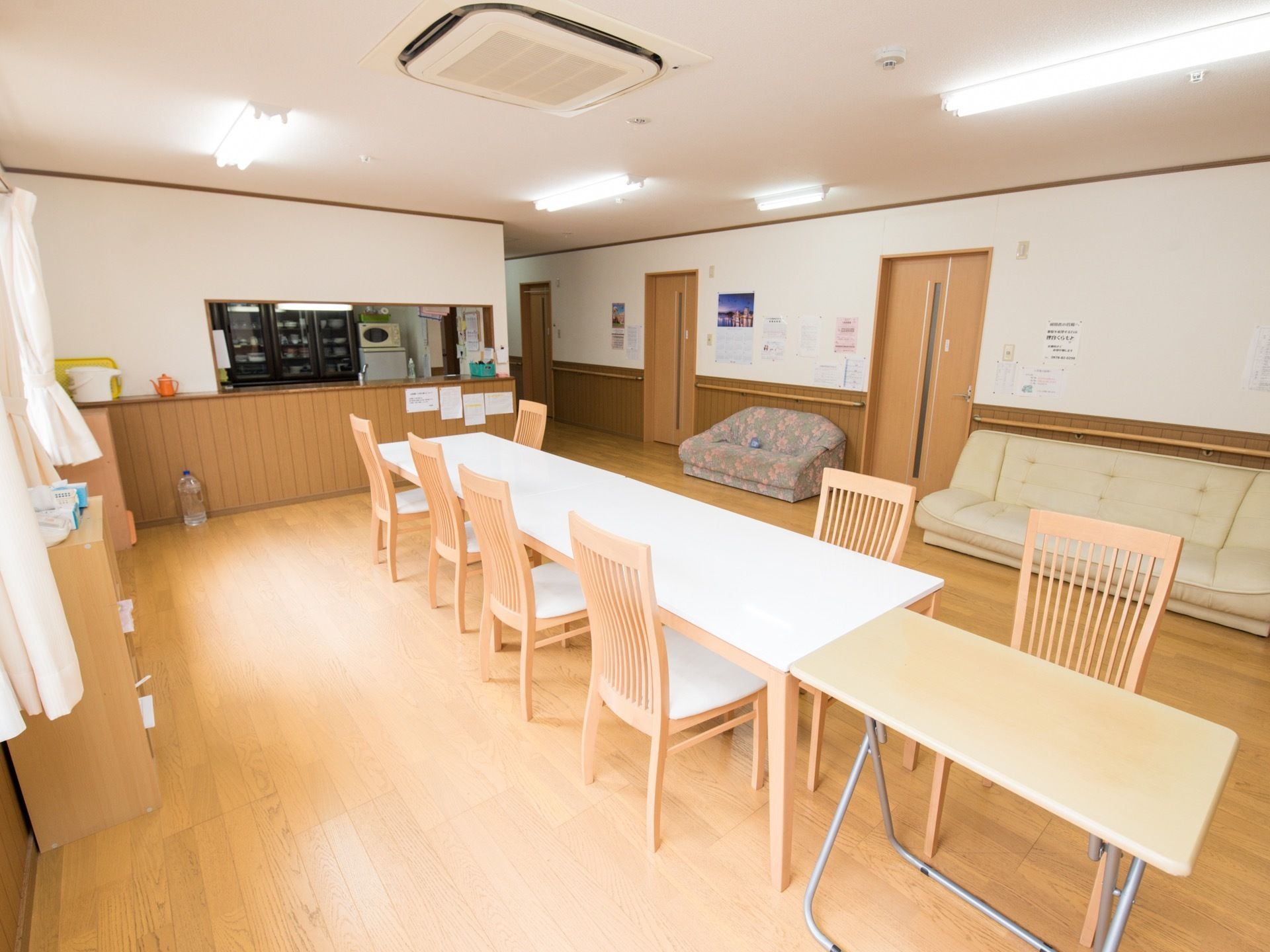 中央に横長のテーブルと1人用のテーブルが並べて置かれている。廊下の壁側に複数のソファーが設置されている。