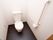 白い壁に黒い床の個室トイレで、掃除が行き届き清潔感がある。左側の壁にL字型の手すりが設置されている。