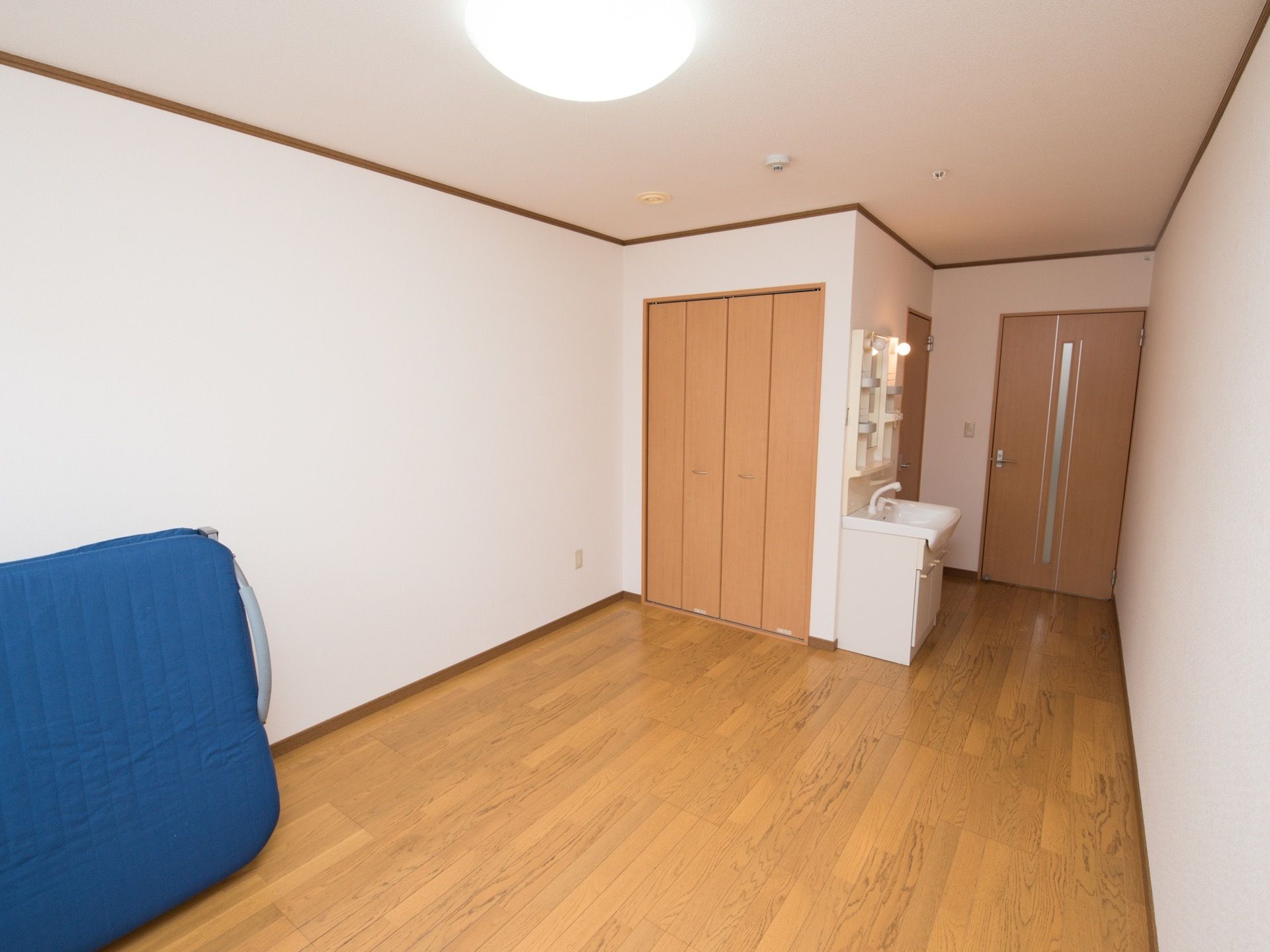 片開きのドアが設置された居室で、左側に洗面台がある。居住スペースに折りたたみ式のベッドが1台用意されている。