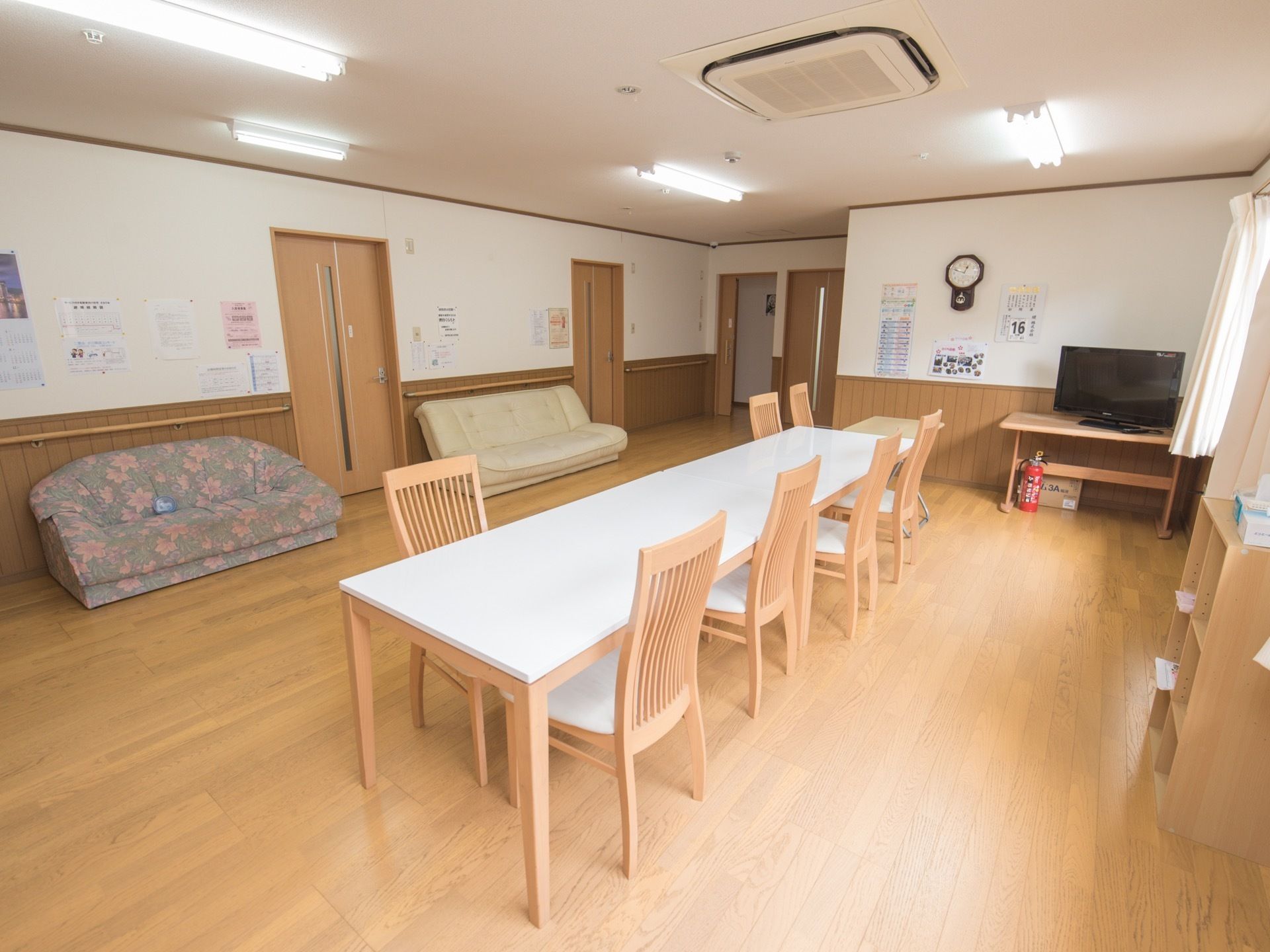 壁側に木製の棚があり、その上にテレビが置かれている。テレビの左側には時計やカレンダーなどが設置されている。