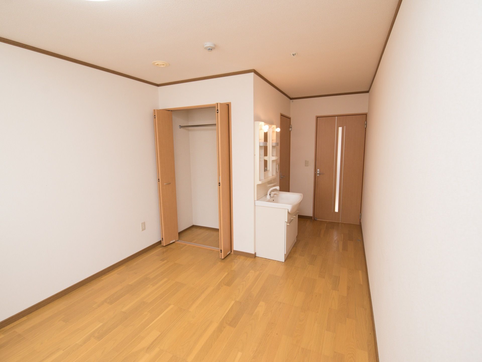 居室のベッドスペース側から見た室内全体の様子。玄関のすぐ横にトイレのドアがあり、そのそばに洗面台と収納が配置されている。