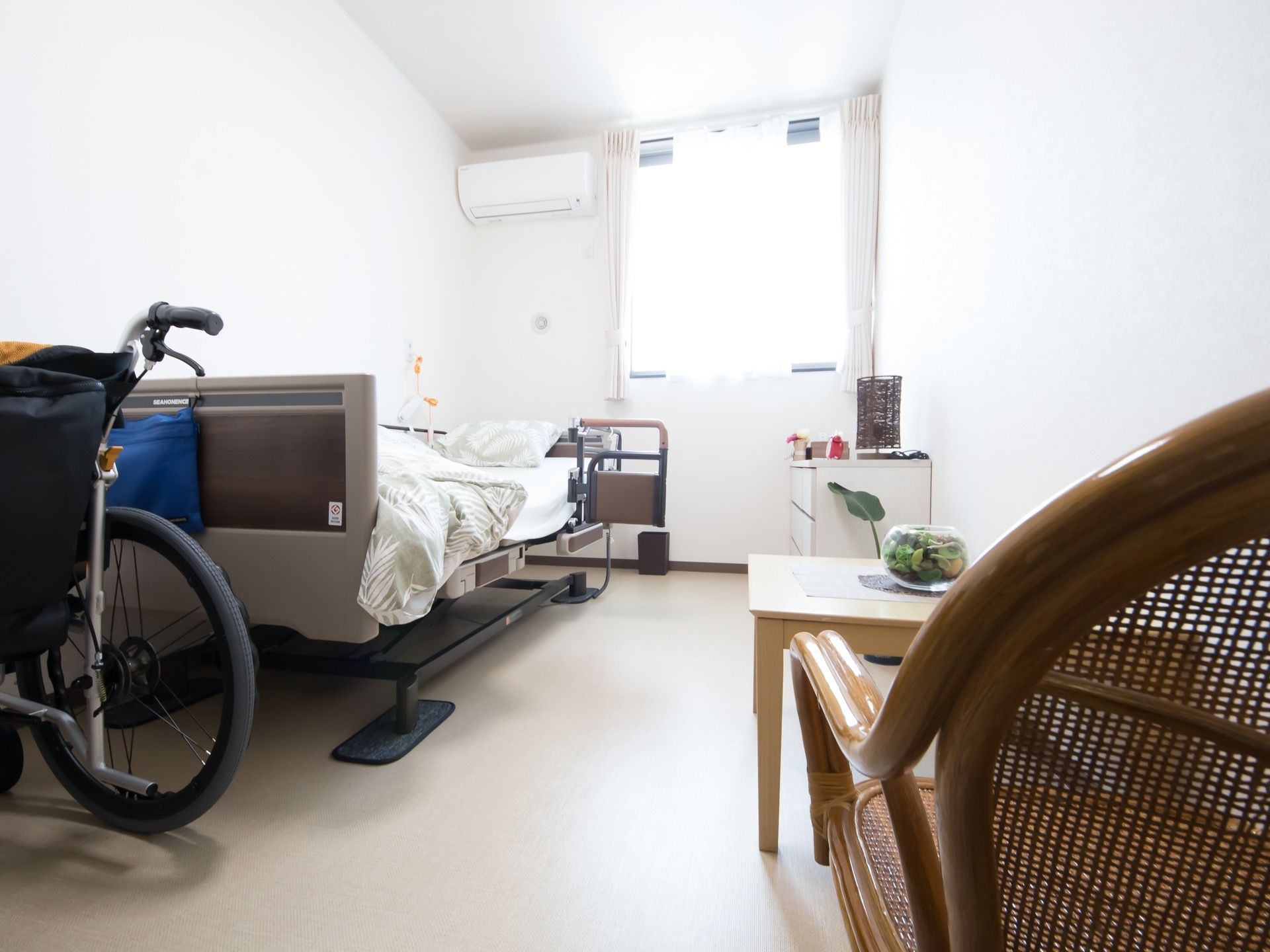 一人部屋タイプの居室である。床はフラットなフローリングになっている。エアコンがあり、壁際にテーブルと椅子が２脚置かれている。