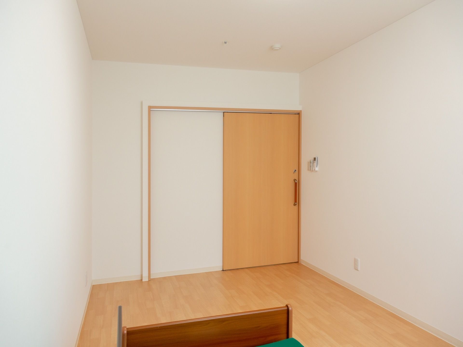 居室の床はフローリングになっている。ドアはスライド式を採用している。ドアの反対側にはベッドが置かれている。