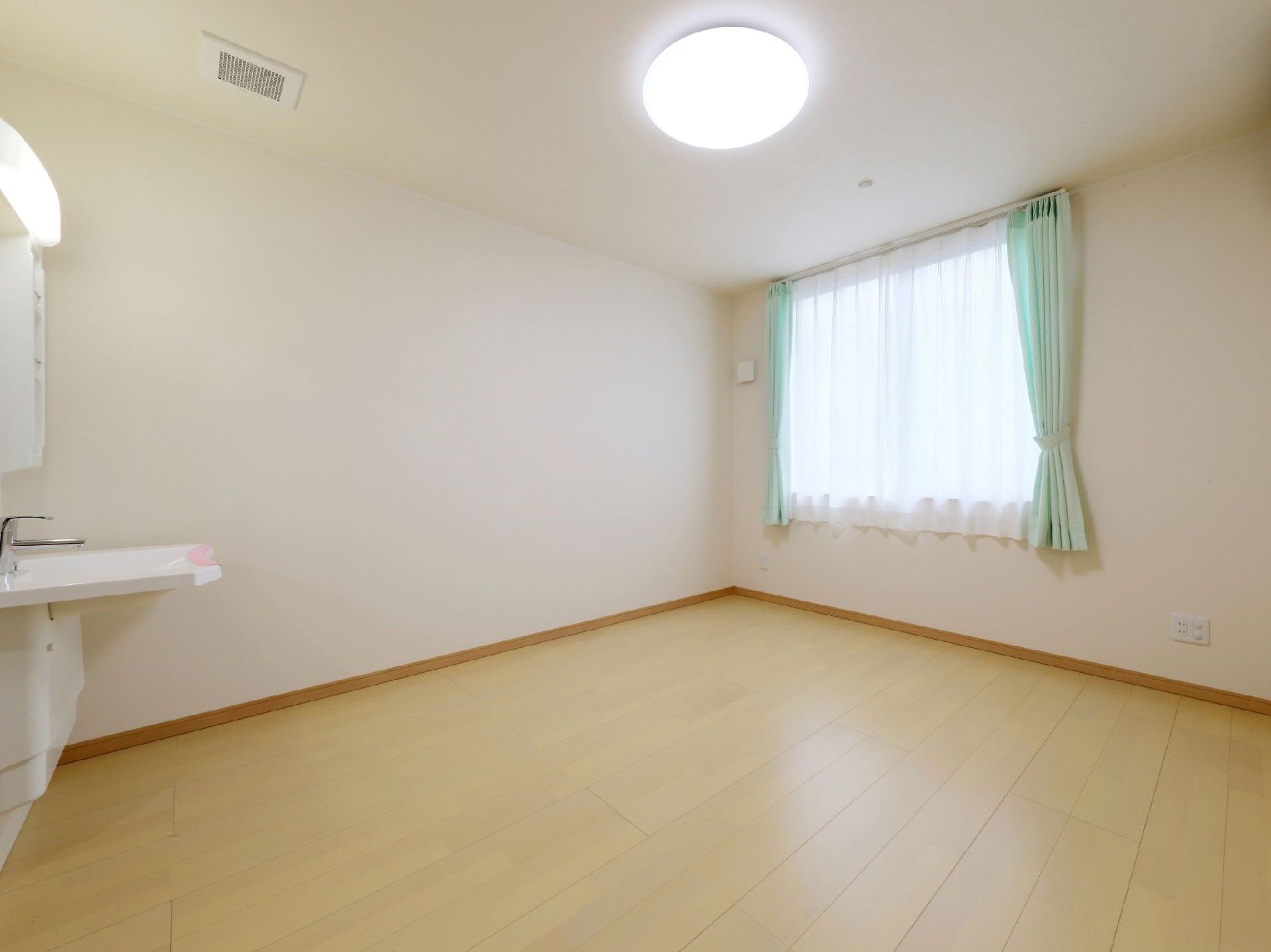 洗面所付きのシンプルなフローリングの居室。窓にはカーテンが付けられている。