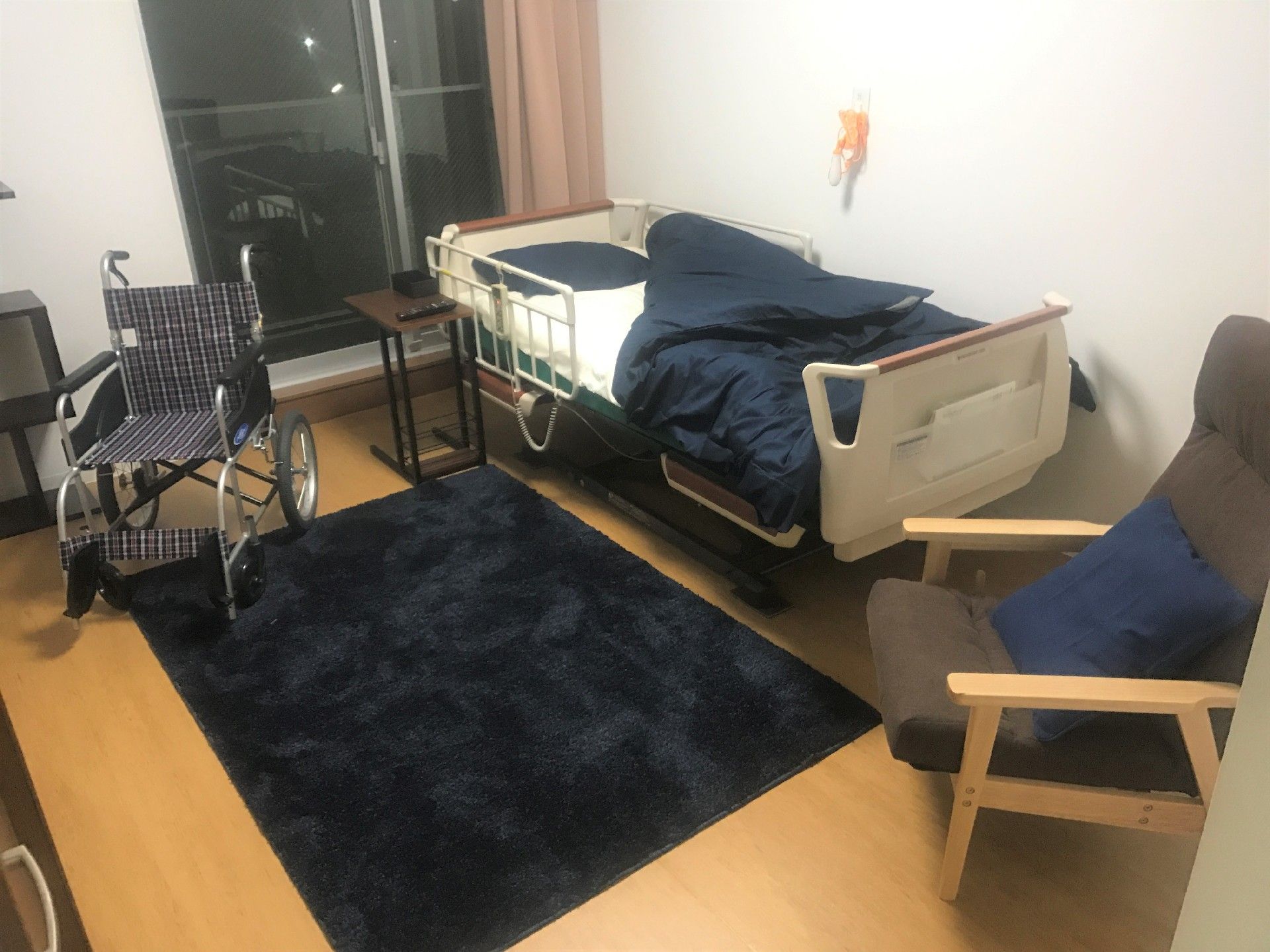 黒いカーペットが中央に如かれ、ベッドサイドにはナースコール。車いすや背もたれ付きのいすも置かれている。