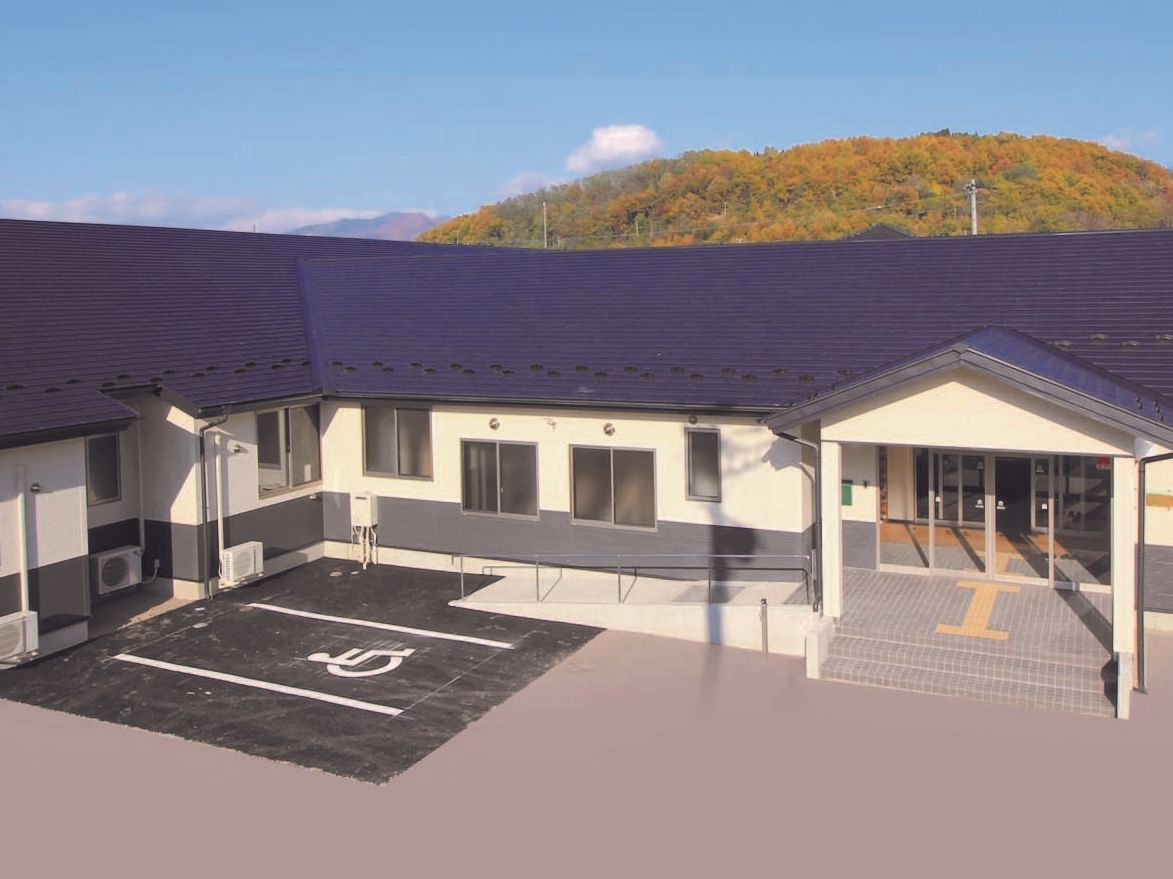 ブルーの屋根をした建物の斜め俯瞰。手前に広々としたスペースがあり、奥には紅葉した山がある。