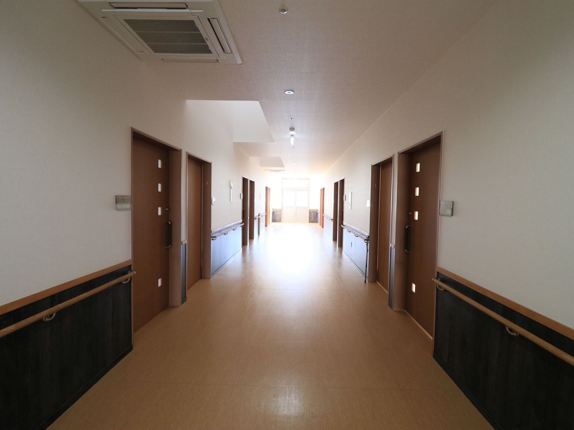白い壁と明るいブラン色の床や建具で統一された、障害物のない廊下である。壁には手すりが設置されている。