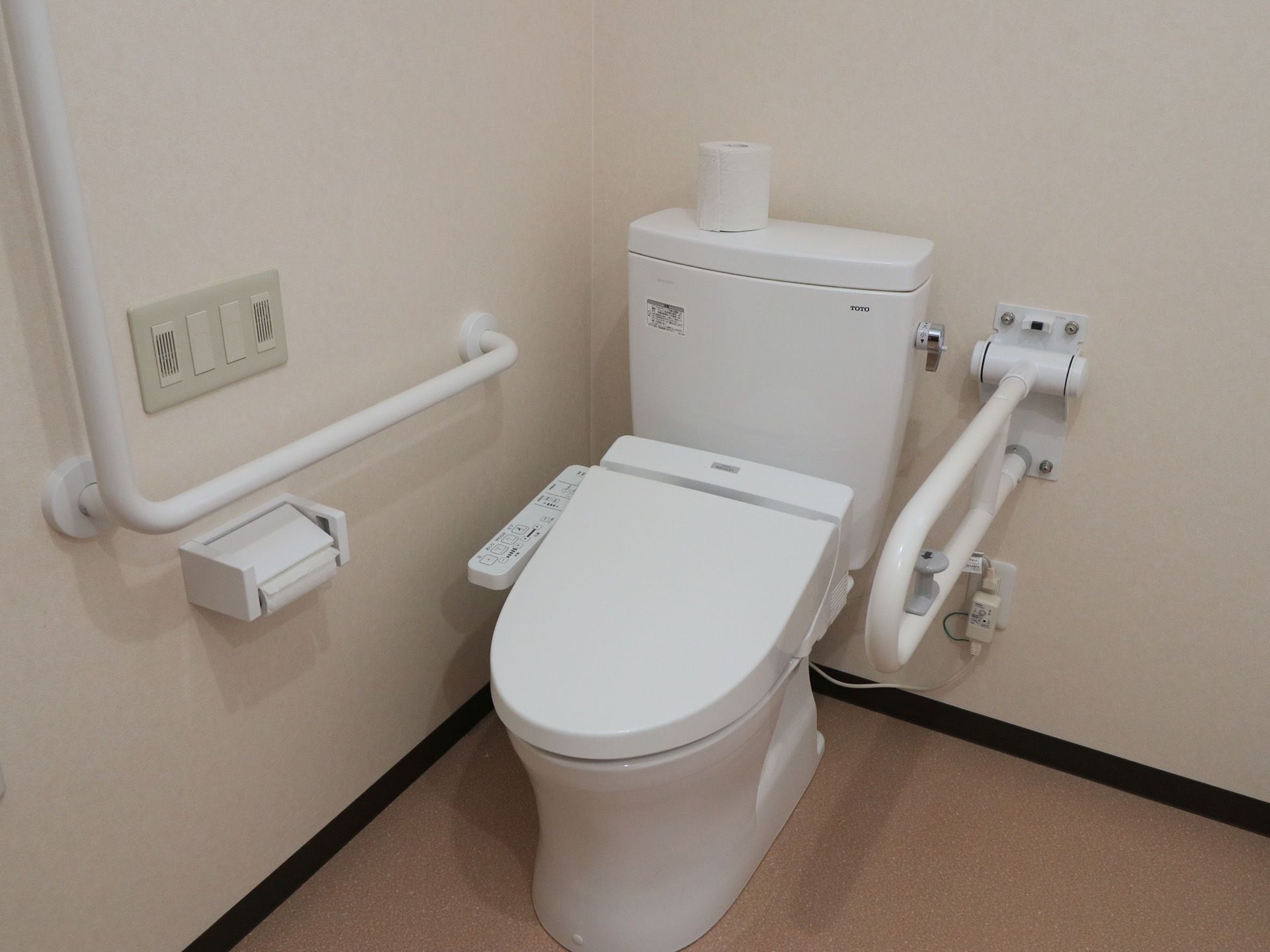 温水洗浄機能付きのトイレが設置されている。壁には可動式の手すりと、Ｌ字型の手すりが取りつけられている。