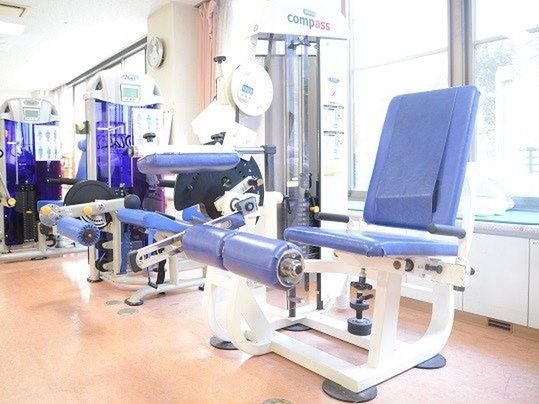 青いリハビリ機器がそろったスペース。壁の一面がほぼ窓となっているため明るい雰囲気。