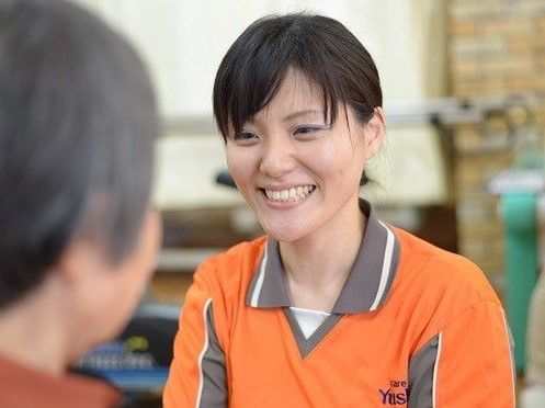 明るい笑顔で入居者に対応している女性スタッフ。オレンジのユニフォームを来ている。