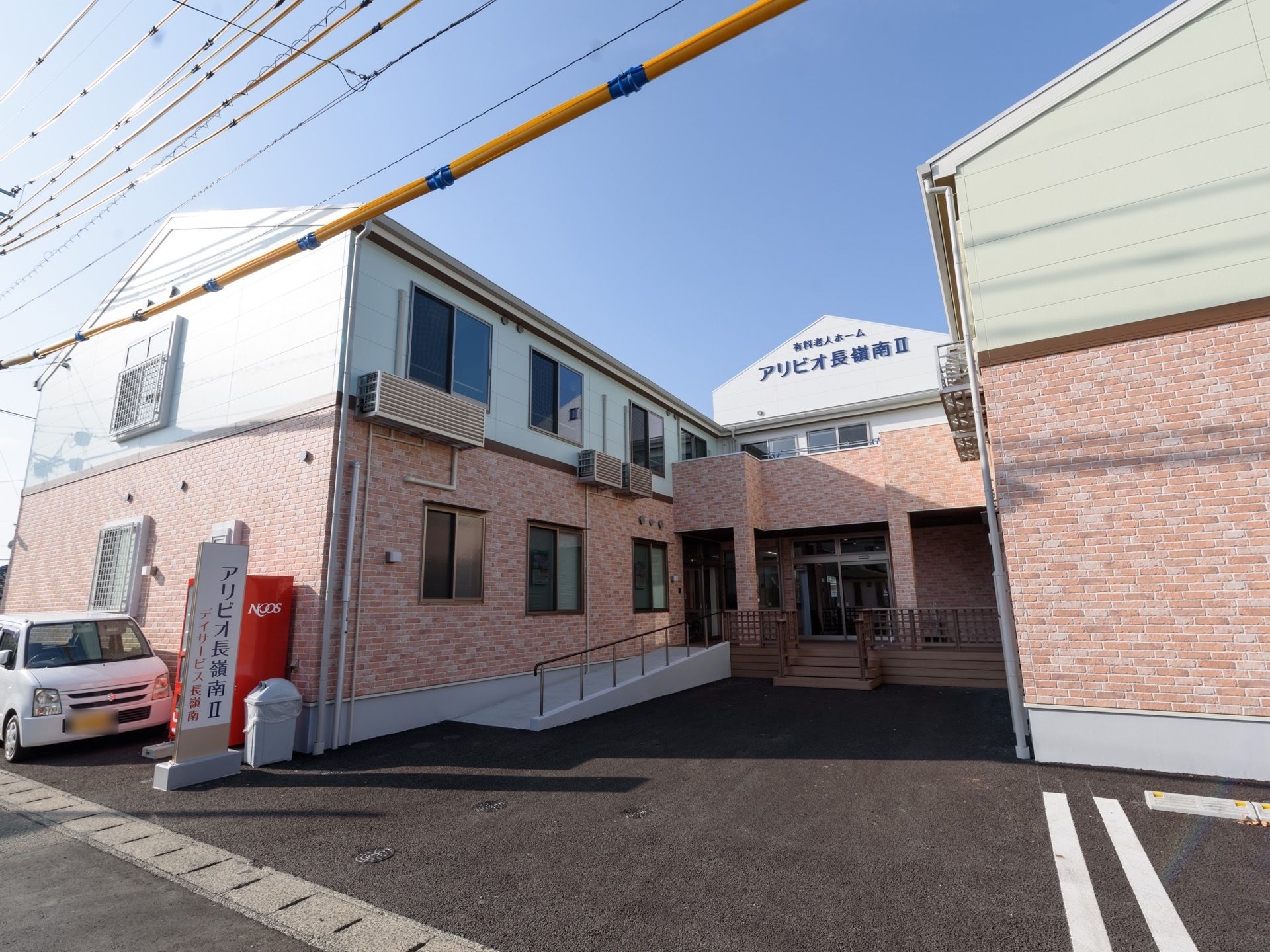アスファルトで整備されている敷地に、コの字型に建物が建てられている。赤い自動販売機の前に白い軽自動車が停められている。