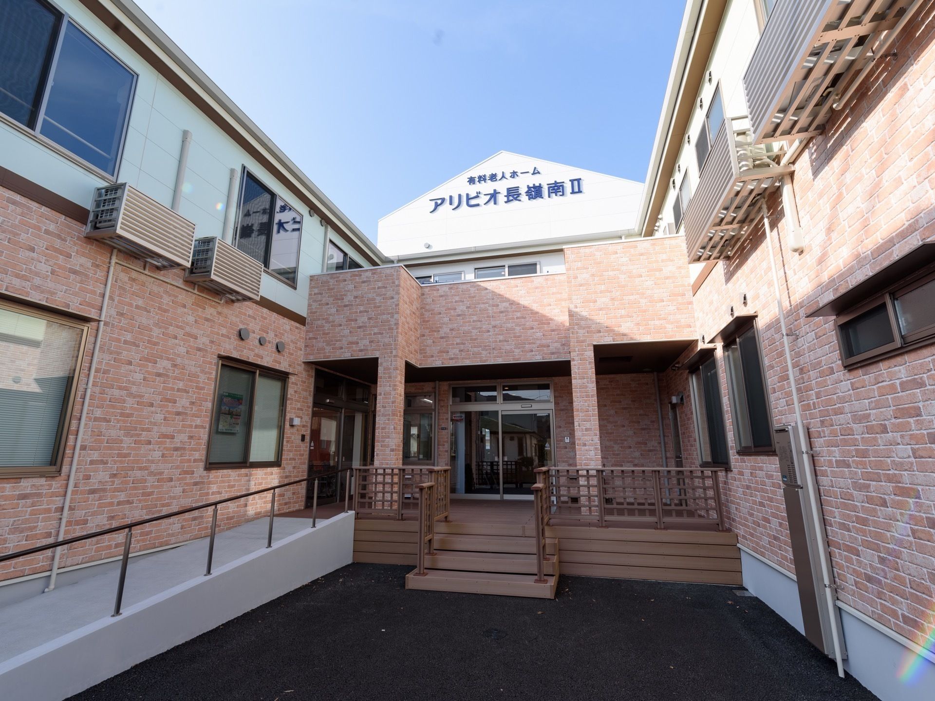 青い空の下にある建物は中央に玄関があり、両サイドに同じ大きさの建物がある。２階建てで駐車スペースも完備。