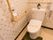 壁にL字型の手すりとナースコールが設置されたトイレがある。洗浄タンクには花が飾られ、壁紙は花柄で明るい空間になっている。