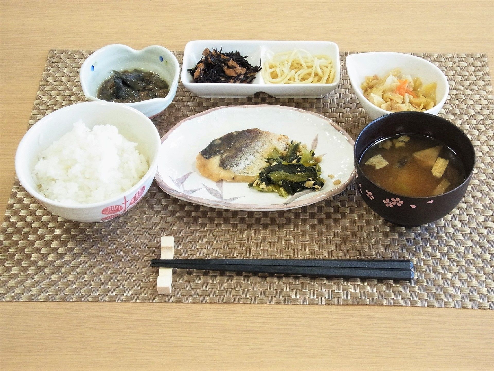 焼き魚に野菜が載ったメニュー。ご飯、味噌汁、漬物などが置かれている