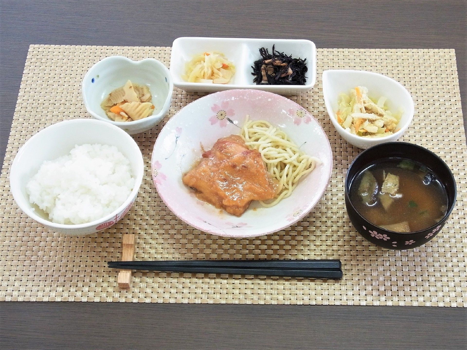 パスタの上に鶏肉が載っているメニュー。ご飯、みそ汁、漬物などが添えられている