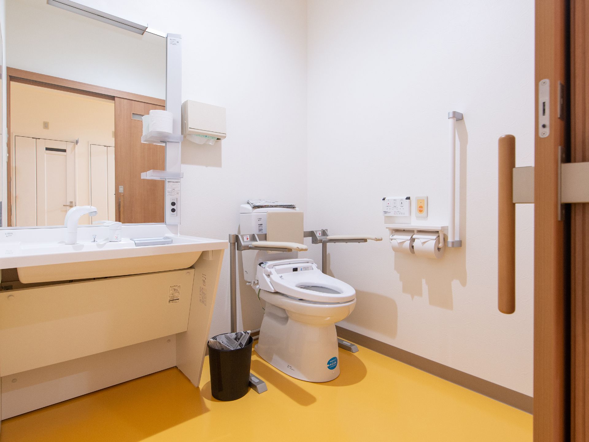 トイレの便座はクッション性ある背もたれに、ひじ掛けが取りつけられている。ゆっくり掛けても体への負担が少ない。